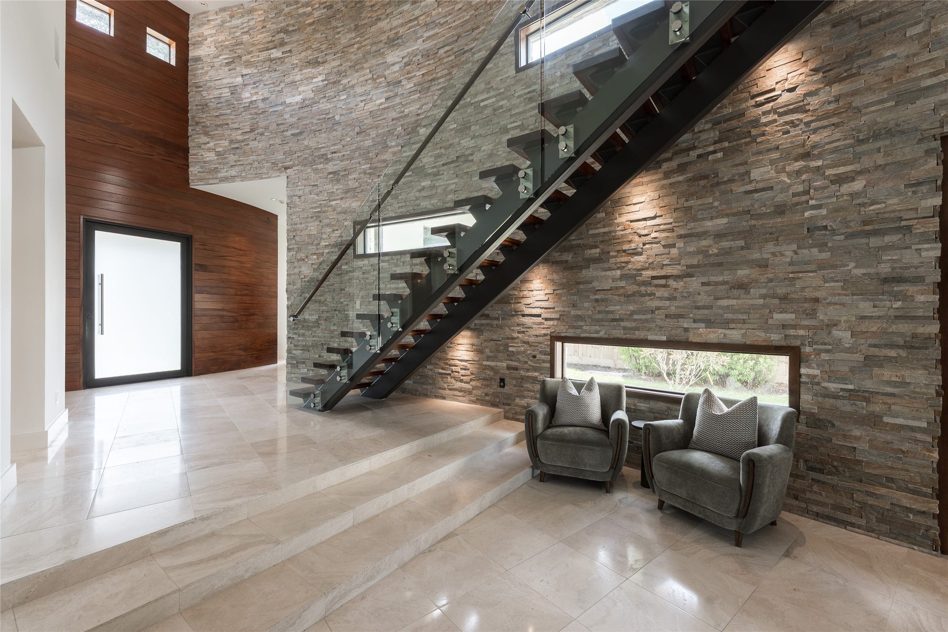 309 Glenwood Drive, Houston, TX 77007 The foyer creates a dramatic sense of arrival through a mahogany-framed 60' pivot door, polished travertine floors and a sculptural curved stacked-stone wall. A subtle step-down transitions from the entry into the main residence, revealing the home gradually rather than all at once.