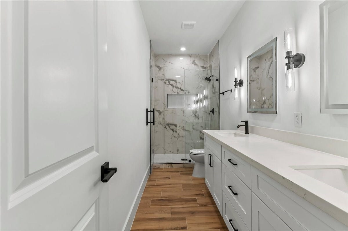 8323 Observatory Street, #A/B, Houston, TX 77088 Unit B - Stylish primary bath is equipped with dual vanities, LED mirrors, and walk-in shower with ceramic tile surround.