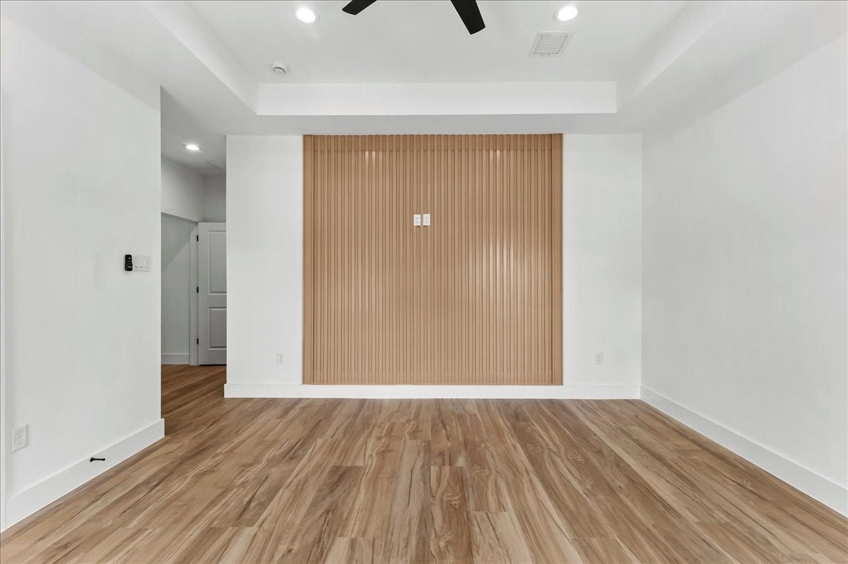 8323 Observatory Street, #A/B, Houston, TX 77088 Unit B - Spacious primary suite featuring a beautiful neutral-toned accent wall that perfectly complements the wood-look flooring, elegant coffered ceiling, and a remote-controlled ceiling fan. Accent Wall design may vary. Pictures are from a previous build.