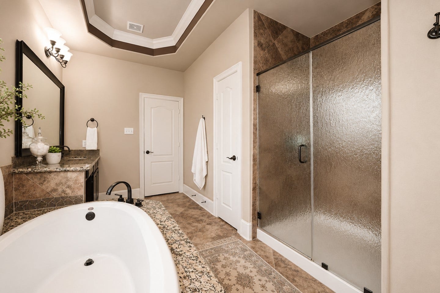 6323 Orange Blossom Lane, Rosenberg, TX 77471 This elegant bathroom features a spacious layout with a luxurious soaking tub, a large glass-enclosed shower, and a dual-sink vanity with granite countertops. The neutral color scheme and detailed tile work add a touch of sophistication.