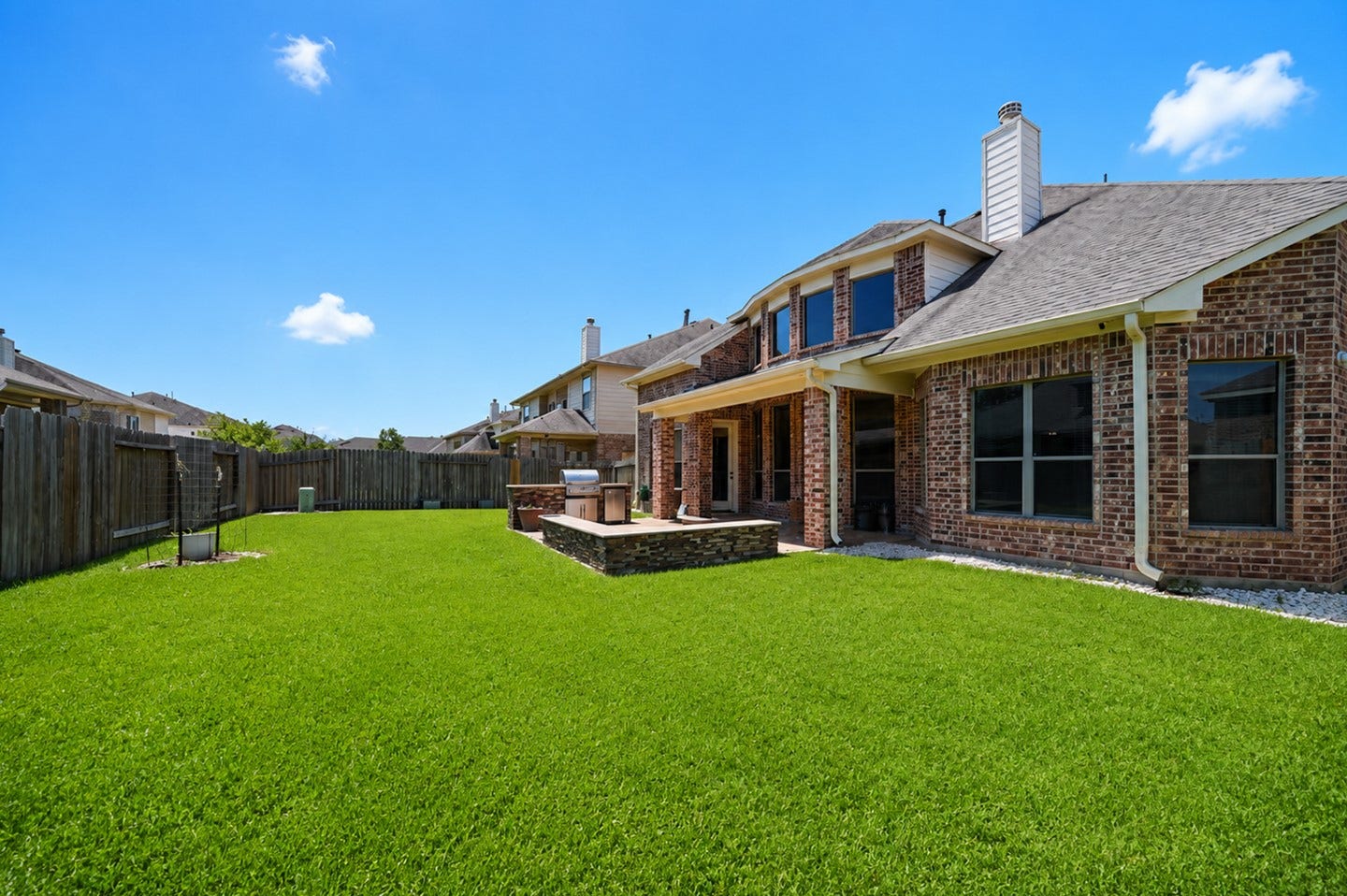 6323 Orange Blossom Lane, Rosenberg, TX 77471 This photo shows the backyard of a brick house with a well-maintained lawn, a spacious patio area, and a wooden fence for privacy, perfect for outdoor activities and entertaining.