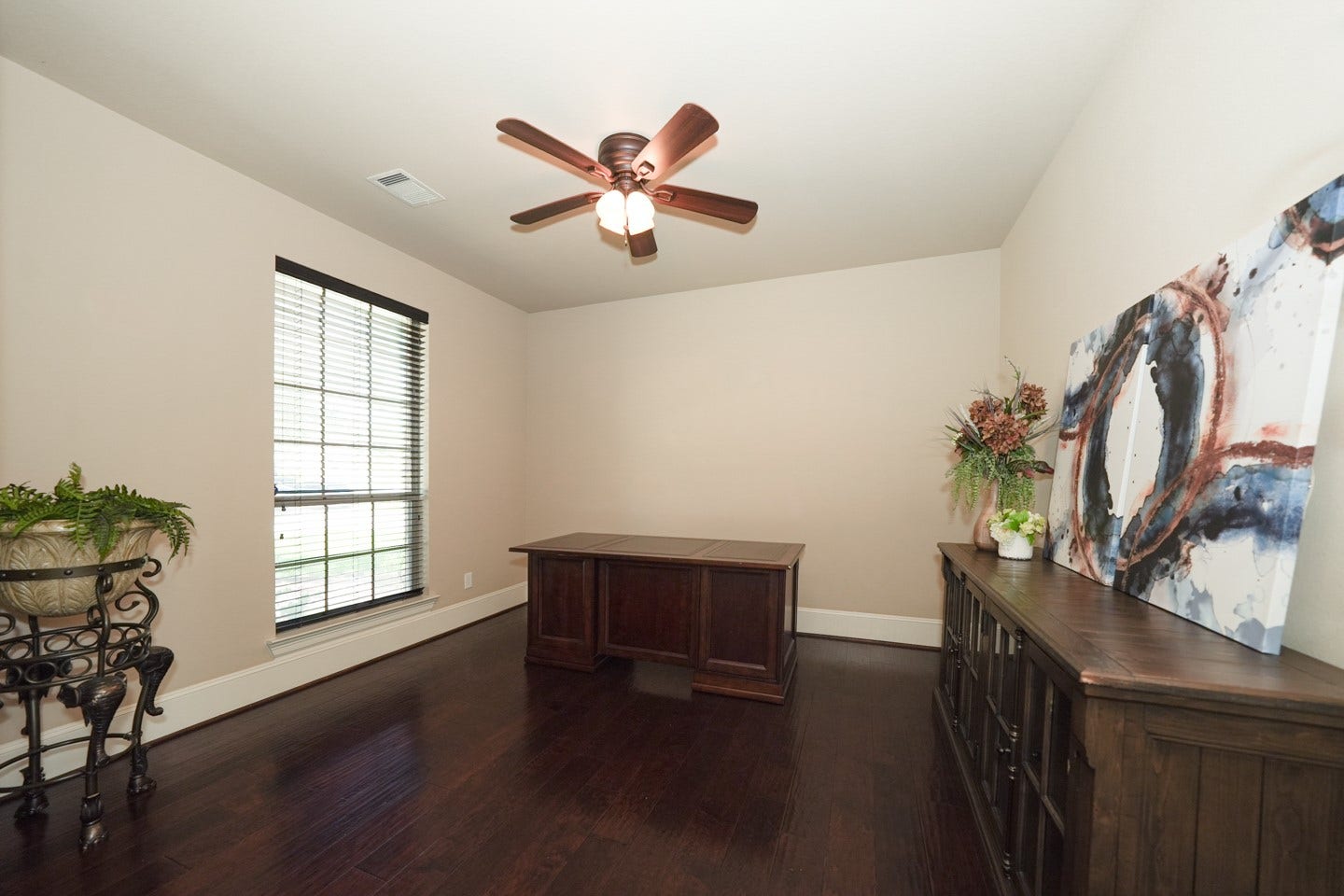 6323 Orange Blossom Lane, Rosenberg, TX 77471 This photo features a bright, spacious office or study space with dark wood flooring and neutral walls. It includes a ceiling fan with a large window.