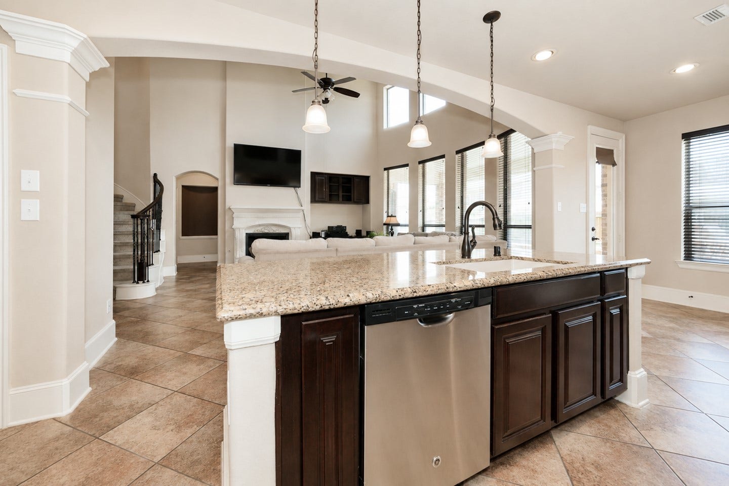 6323 Orange Blossom Lane, Rosenberg, TX 77471 This modern open-concept living space features a spacious kitchen with granite countertops, pendant lighting, and stainless-steel appliances. It flows into a bright living area with high ceilings, large windows, and a fireplace, creating a welcoming atmosphere.