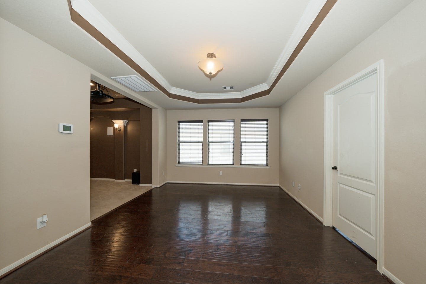 6323 Orange Blossom Lane, Rosenberg, TX 77471 This flex room features dark hardwood floors, a tray ceiling and a large window for natural light. It offers a spacious, open feel with an adjacent area visible through a wide doorway.
