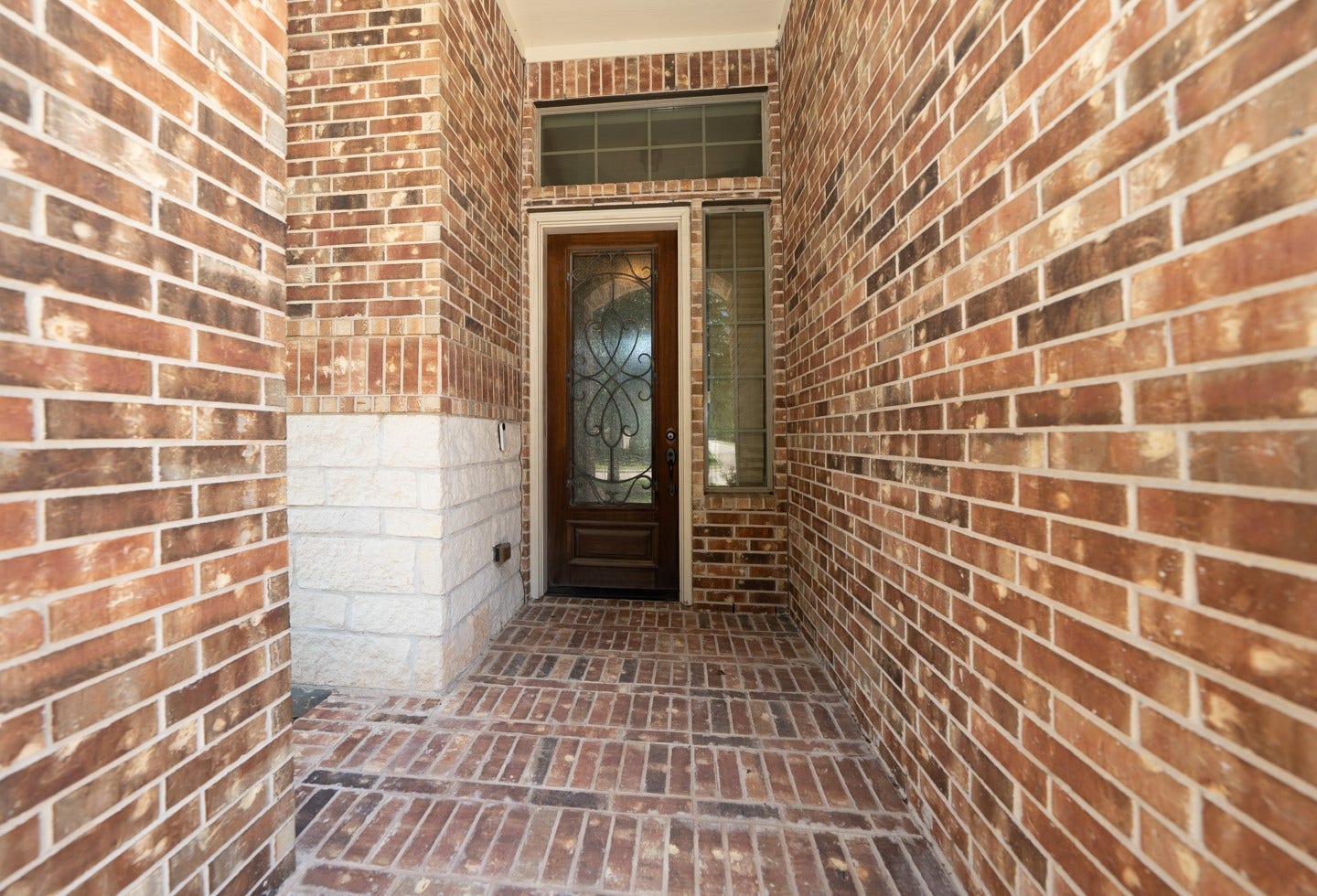 6323 Orange Blossom Lane, Rosenberg, TX 77471 This photo showcases a welcoming entryway with a decorative wooden front door featuring glass panels. The surrounding walls and floor are made of red brick, offering a warm and classic look.