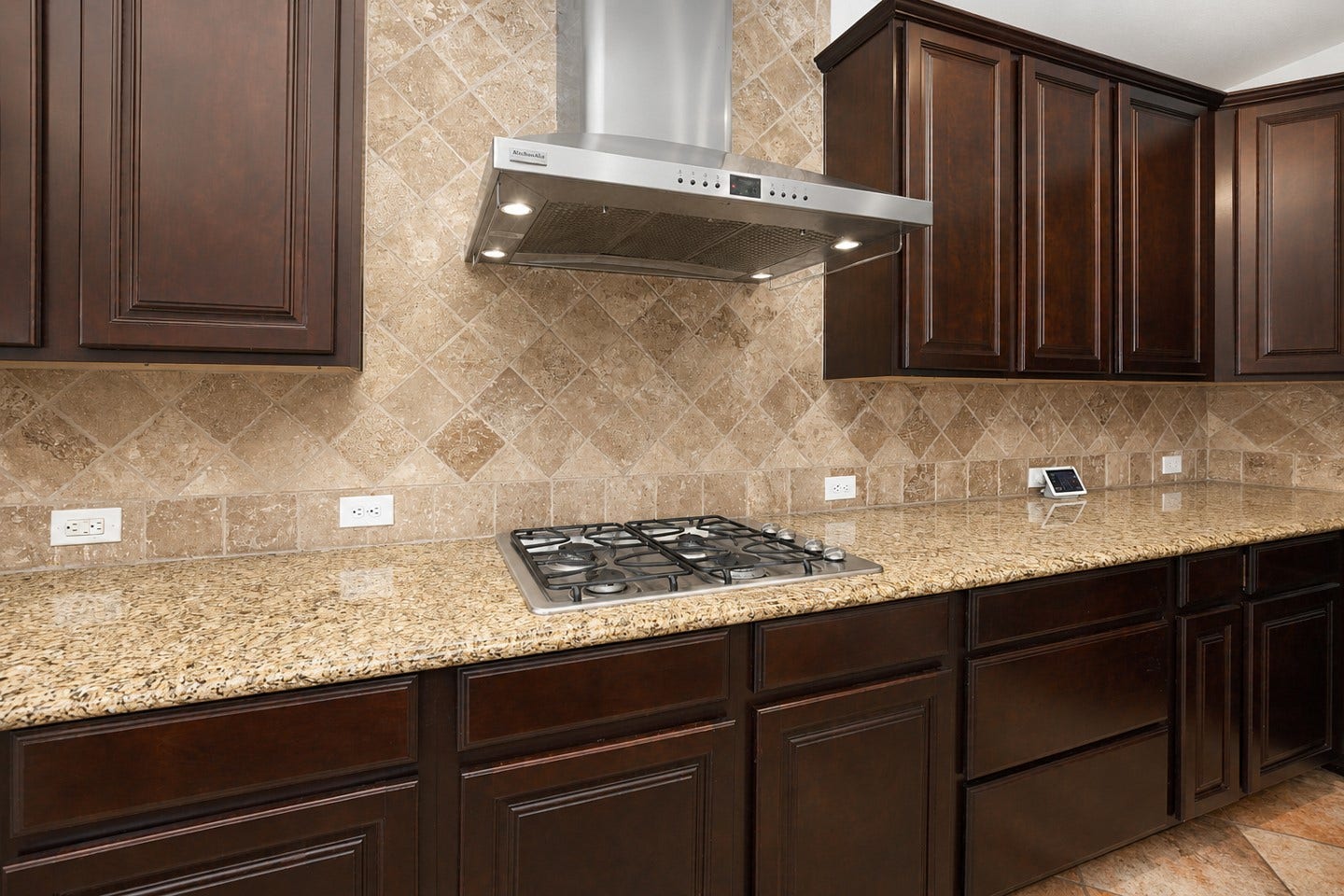 6323 Orange Blossom Lane, Rosenberg, TX 77471 This kitchen features rich dark wood cabinets, a sleek stainless steel range hood, granite countertops, and a stylish tiled backsplash, offering a blend of elegance and functionality.