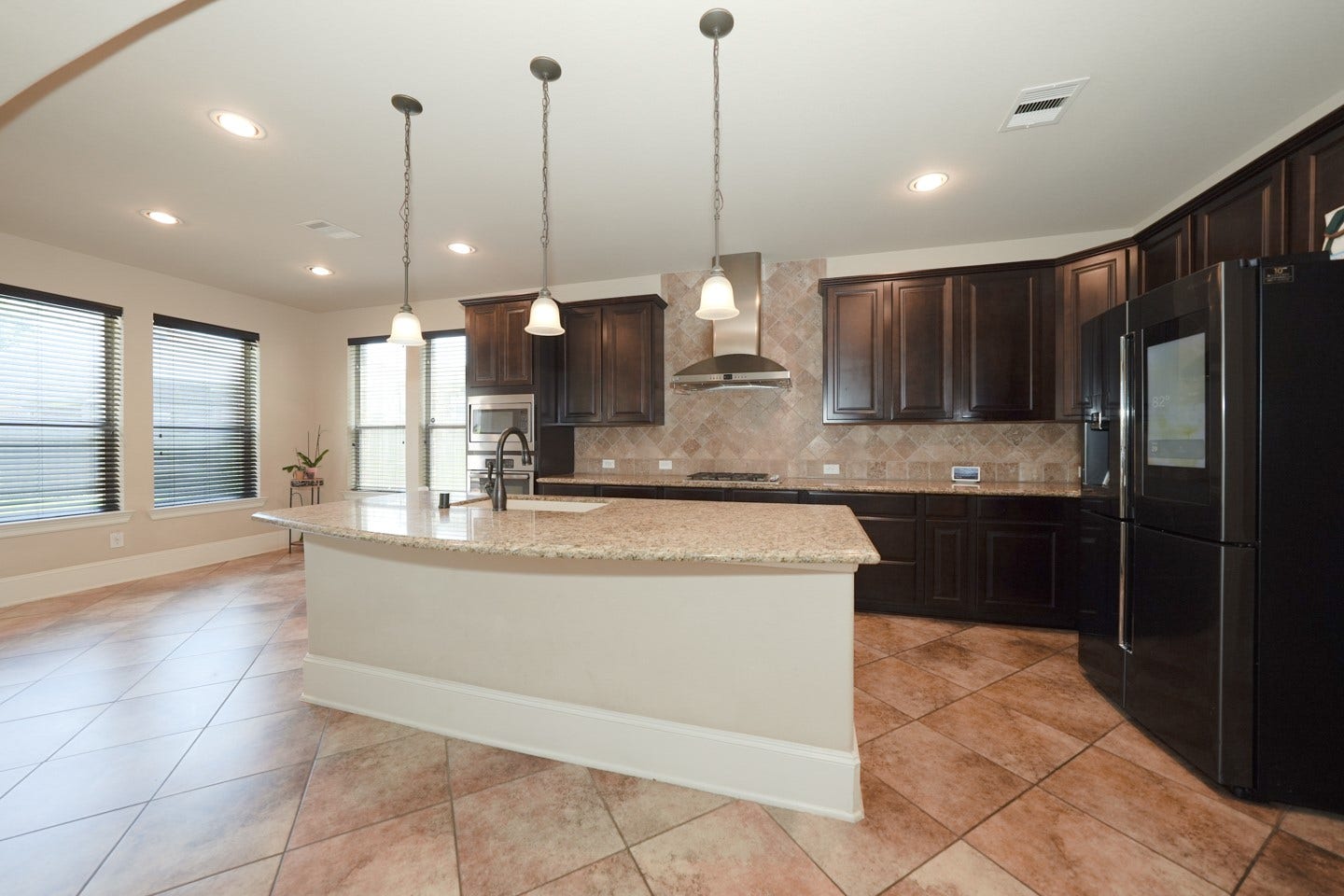 6323 Orange Blossom Lane, Rosenberg, TX 77471 This spacious kitchen features dark wood cabinetry, a large granite island and pendant lighting. The open layout is accented by tiled flooring and ample natural light from multiple windows.