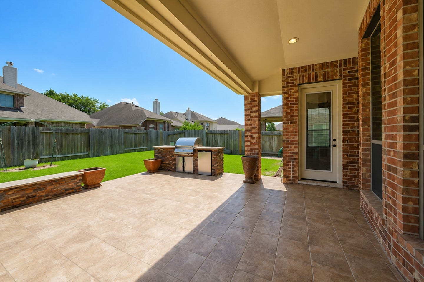 6323 Orange Blossom Lane, Rosenberg, TX 77471 This photo showcases a spacious covered patio with tile flooring, a built-in grill, and a view of a well-maintained fenced backyard. Perfect for outdoor entertaining and relaxation.