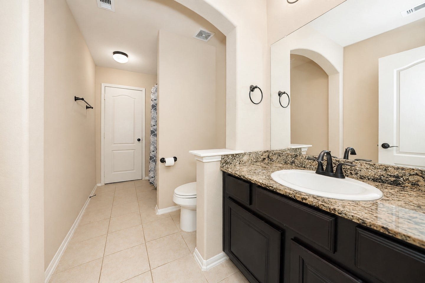 6323 Orange Blossom Lane, Rosenberg, TX 77471 This bathroom features a spacious layout with a granite countertop, dark wood vanity, and a large mirror. It has a tiled floor and the Neutral tones create a warm and inviting atmosphere.