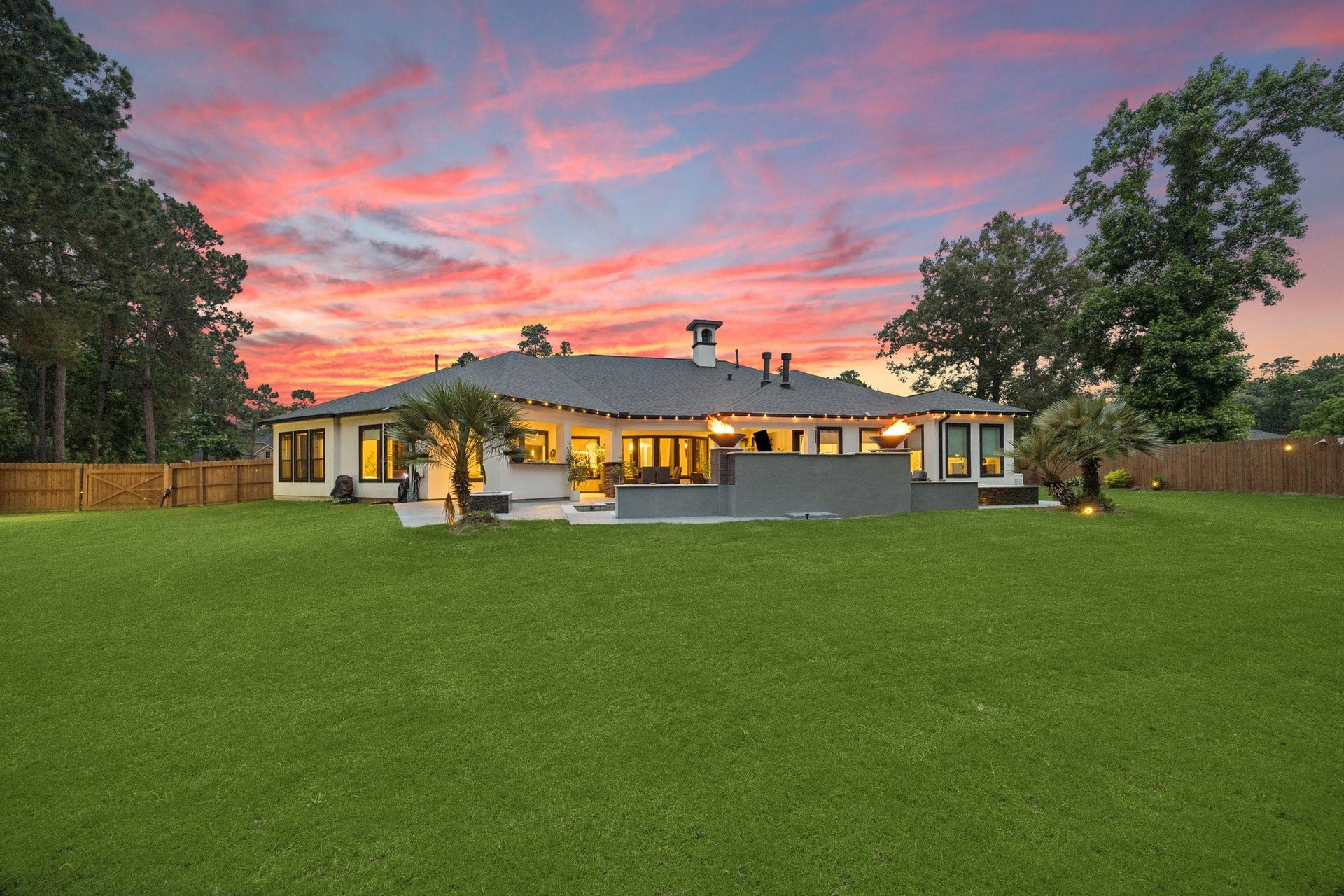 27303 E Benders Landing Boulevard, Spring, TX 77386 Stunning evening view of the backyard showcases the inviting atmosphere of the outdoor living space, where the illuminated patio, resort-style pool, and lawn come together to create a warm and relaxing setting for unwinding beneath the evening sky.
