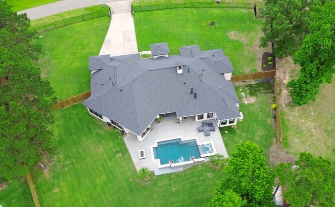 27303 E Benders Landing Boulevard, Spring, TX 77386 Birds-eye view captures the exceptional layout of the property, showcasing the seamless blend of luxury outdoor living and open green space. The thoughtfully designed backyard offers a spacious patio, inviting pool and spa, and an expansive lawn wit room for play, sports, entertainment, or future outdoor enhancements.