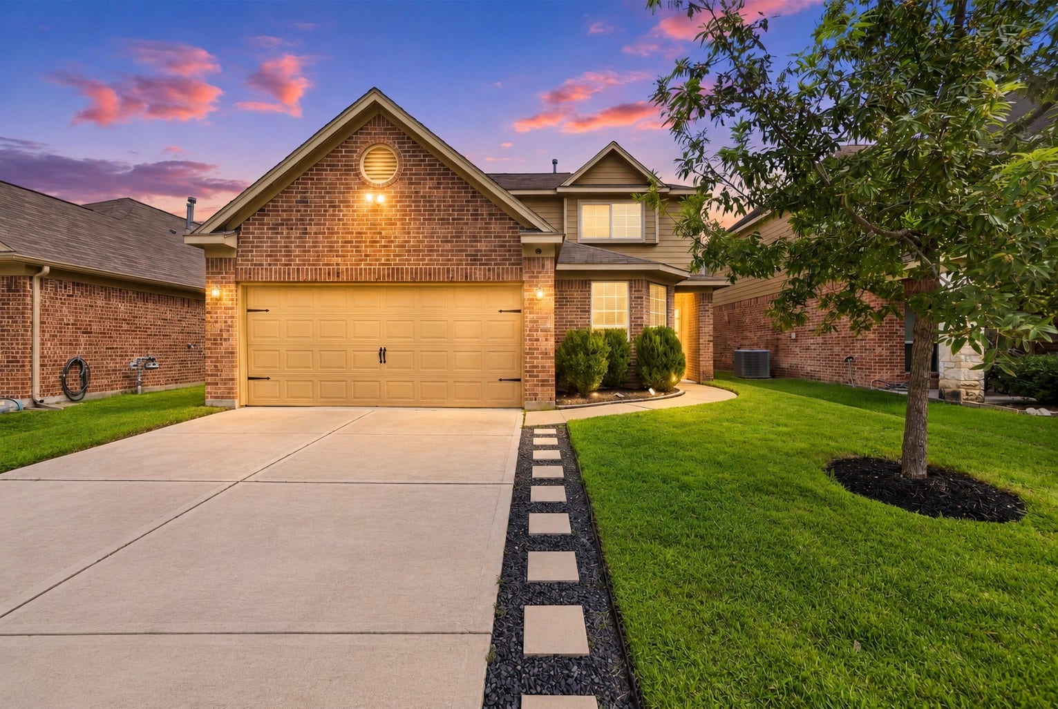 Twilight Exterior: Beautiful twilight view showcasing the homes brick exterior, inviting entry, two-car garage, manicured lawn, and warm exterior lighting.