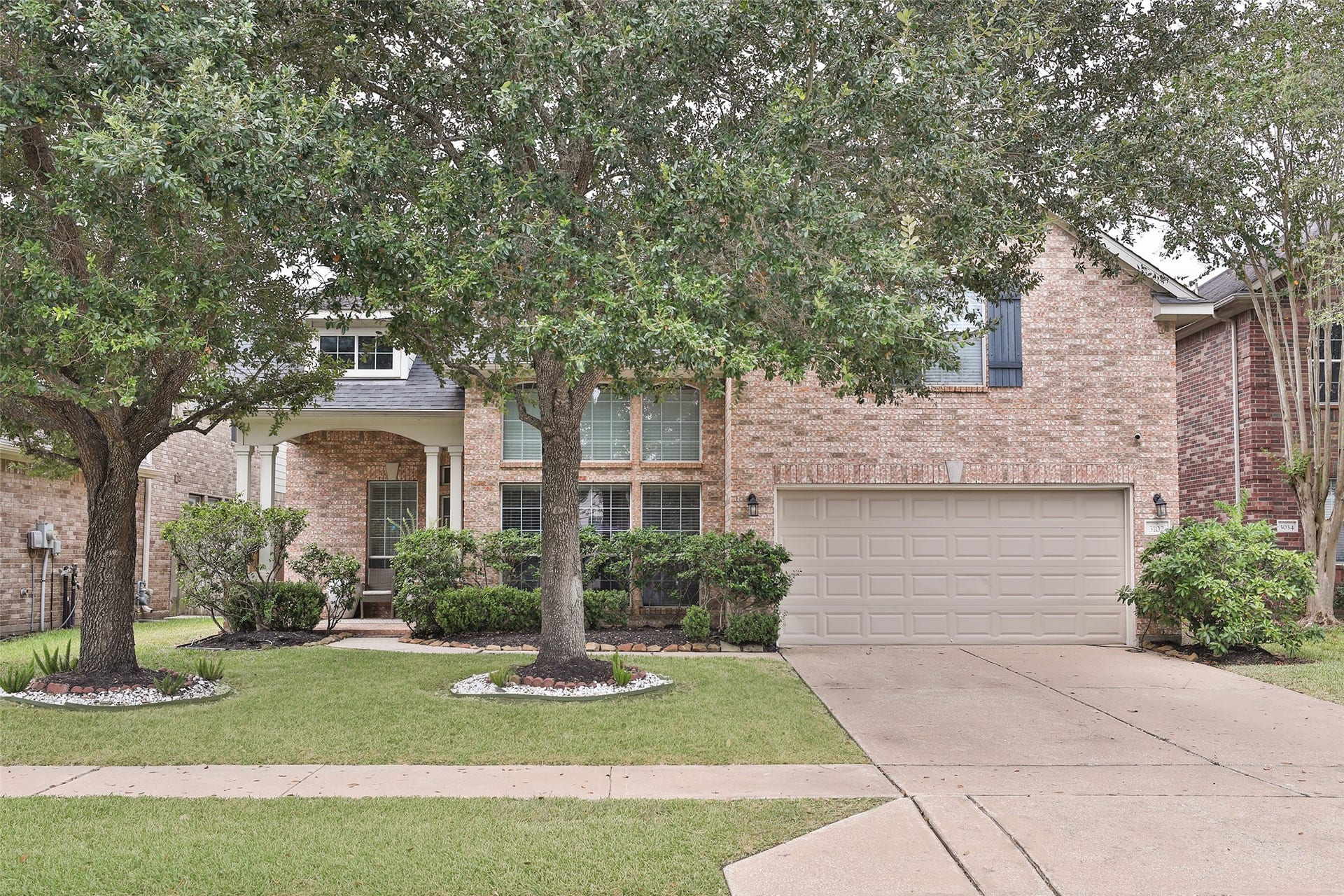 3102 Palm Harbour Drive, Missouri City, TX 77459 Charming two-story brick home with a spacious two-car garage, framed by mature trees and lush landscaping, offering great curb appeal.