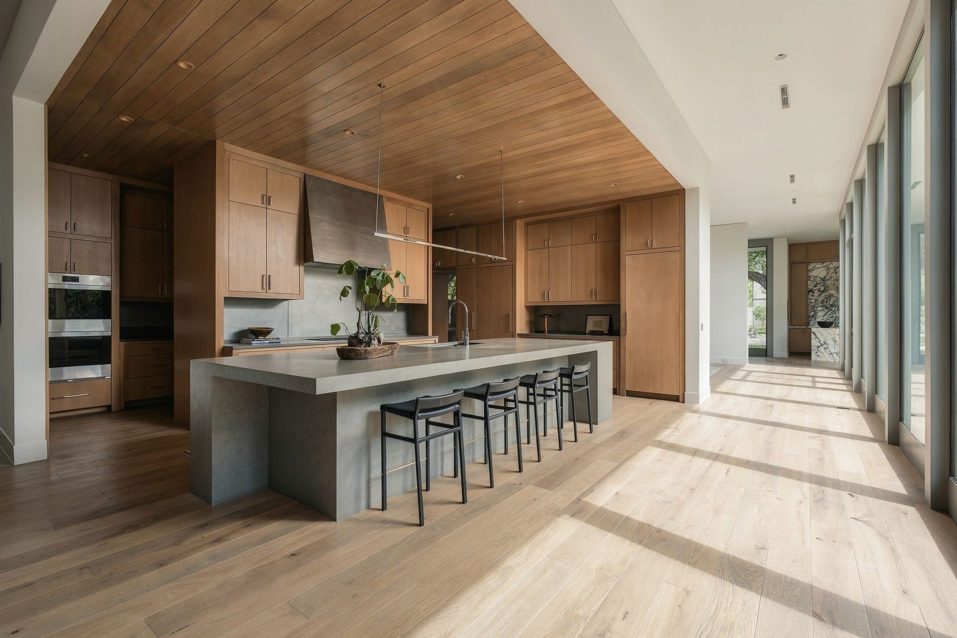 Looking back toward the entry, the kitchen becomes part of the homes long architectural sight line. Rift white oak cabinetry & warm European white oak floors contrast beautifully w/the gallery of glass, allowing natural light & views of the landscape to remain central to the experience of the home.