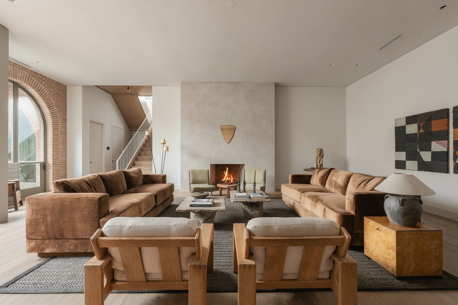 Spacious family room anchored by a striking diamond-plaster gas fireplace w/custom concrete-finished interior. The sculptural staircase rises just beyond, while an arched opening leads to the covered back porch, continuing the homes signature architectural language from inside to out.