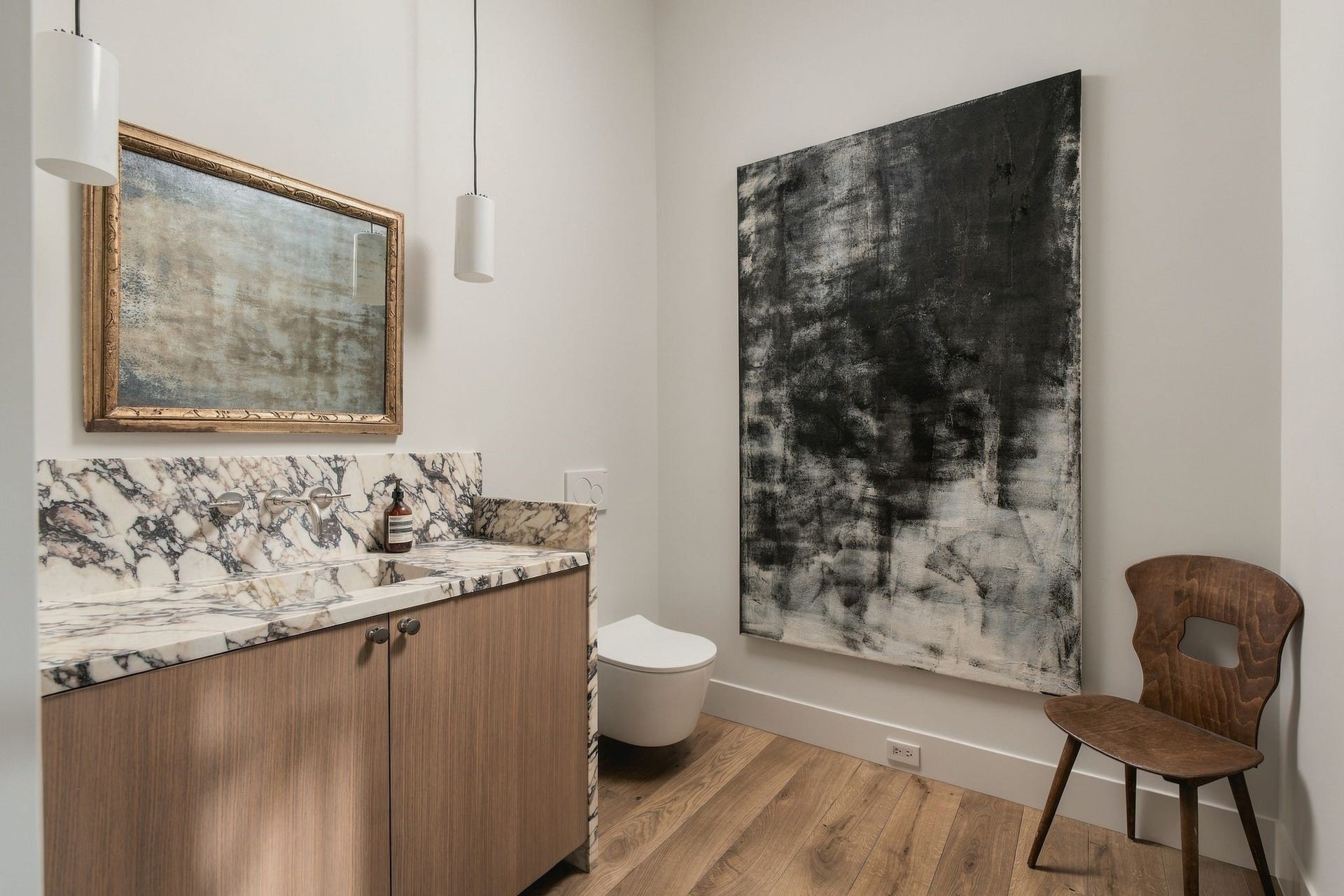A true jewel-box powder room. Richly veined Calacatta Monet extends across the countertop & backsplash w/an integrated marble sink, paired w/a wall-mounted Watermark polished nickel faucet, Toto wall-mounted toilet & sculptural Santa & Cole pendant lighting.