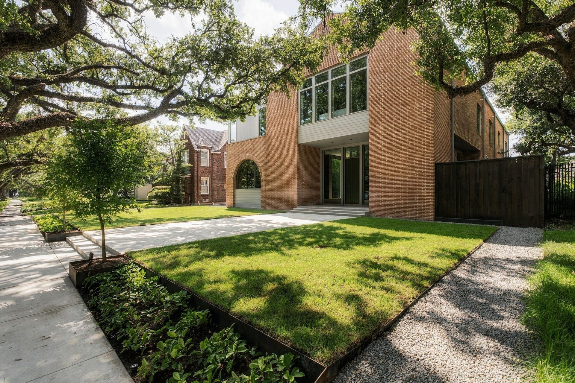 A closer look at the craftsmanship defining The Arch House. Arched details, Mid-Century elongated brick & warm wood siding are framed by mature trees, layered landscaping & exterior lighting. No traditional window trimthe siding itself changes direction & plane to frame the openings, adding subtle depth to the faade.