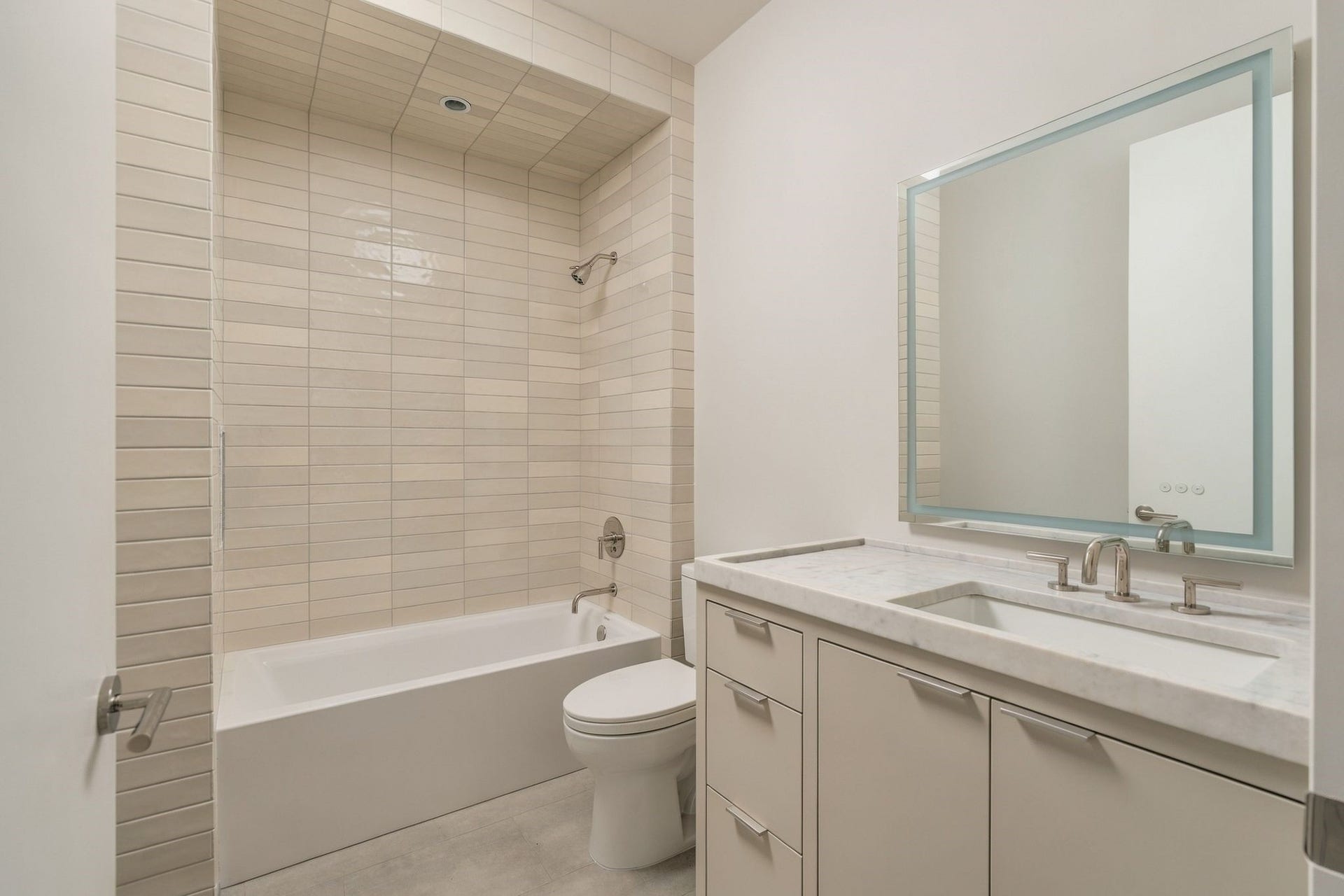 Beautifully finished en suite guest bath continues the homes refined material palette w/porcelain tile, generous vanity storage, polished nickel hardware & illuminated mirrorgiving each secondary suite the privacy & finish quality expected of a custom-level home.