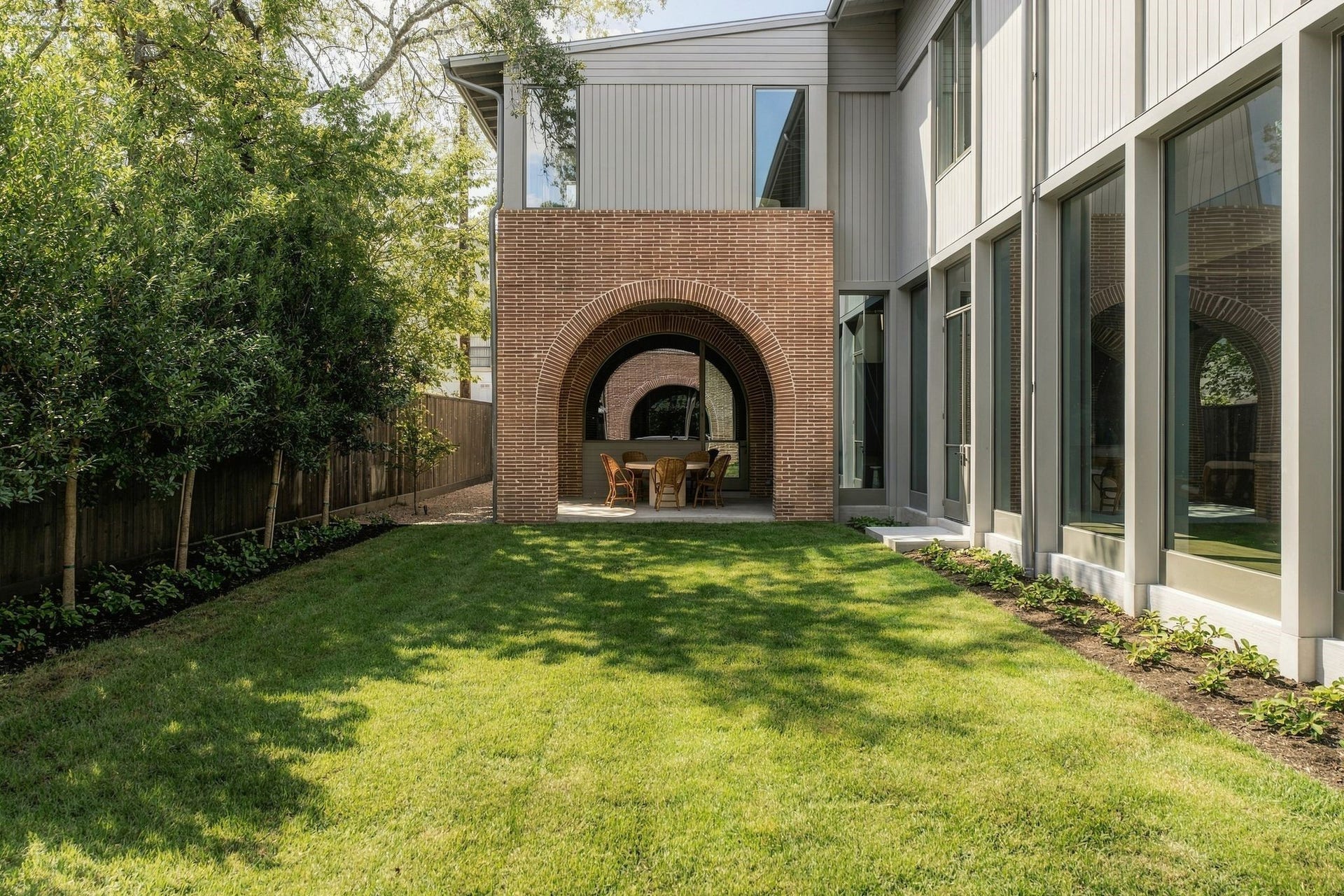 Perfect symmetry defines the rear elevation, where a series of beautifully proportioned arches creates a striking covered outdoor living space. The architectural motif introduced at the front of the home continues here, creating a cohesive dialogue between the house, covered porch & landscape.
