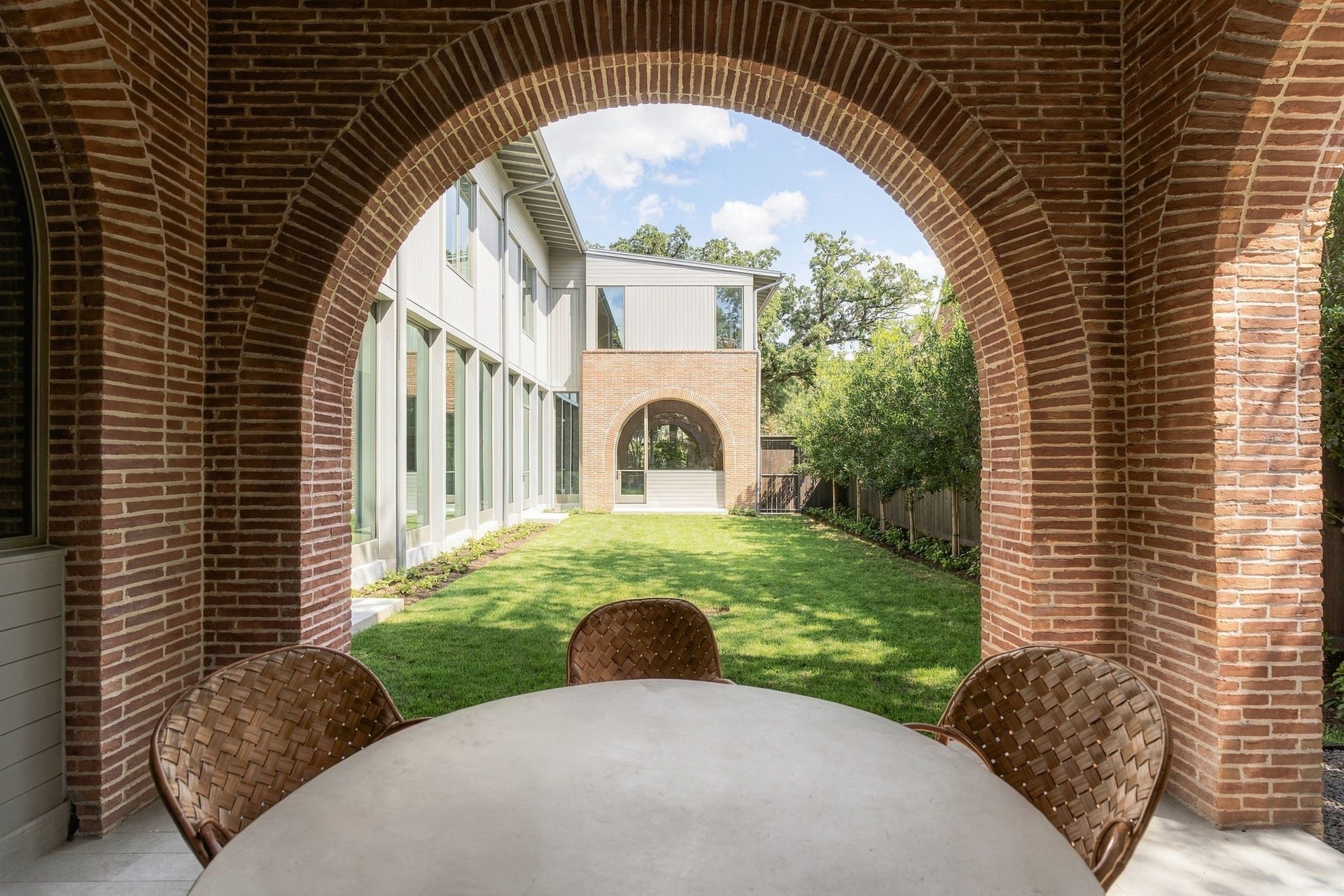 The homes architecture unfolds naturally outdoors. From the covered back porch, repeating arches frame views across the expansive lawn while Mid-Century elongated brick carries the exterior palette through the entertaining spaces. Ample room for outdoor dining & lounging creates an effortless extension of the interiors.