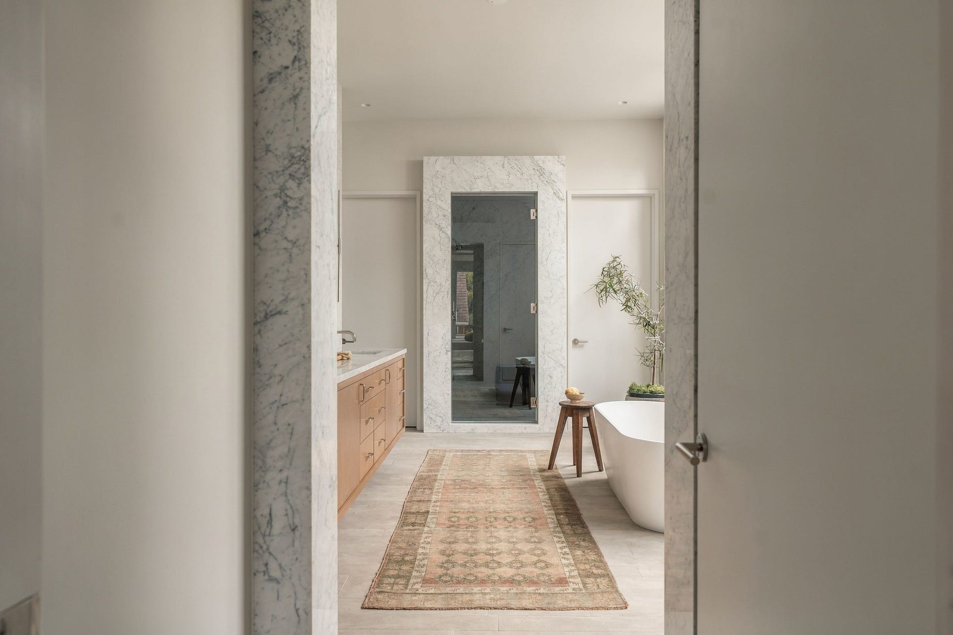 A dramatic marble-cased entry introduces the primary bath, immediately framing the matching marble-surrounded shower beyond. The carefully composed sight line offers another example of the disciplined proportion & material continuity found throughout the home.