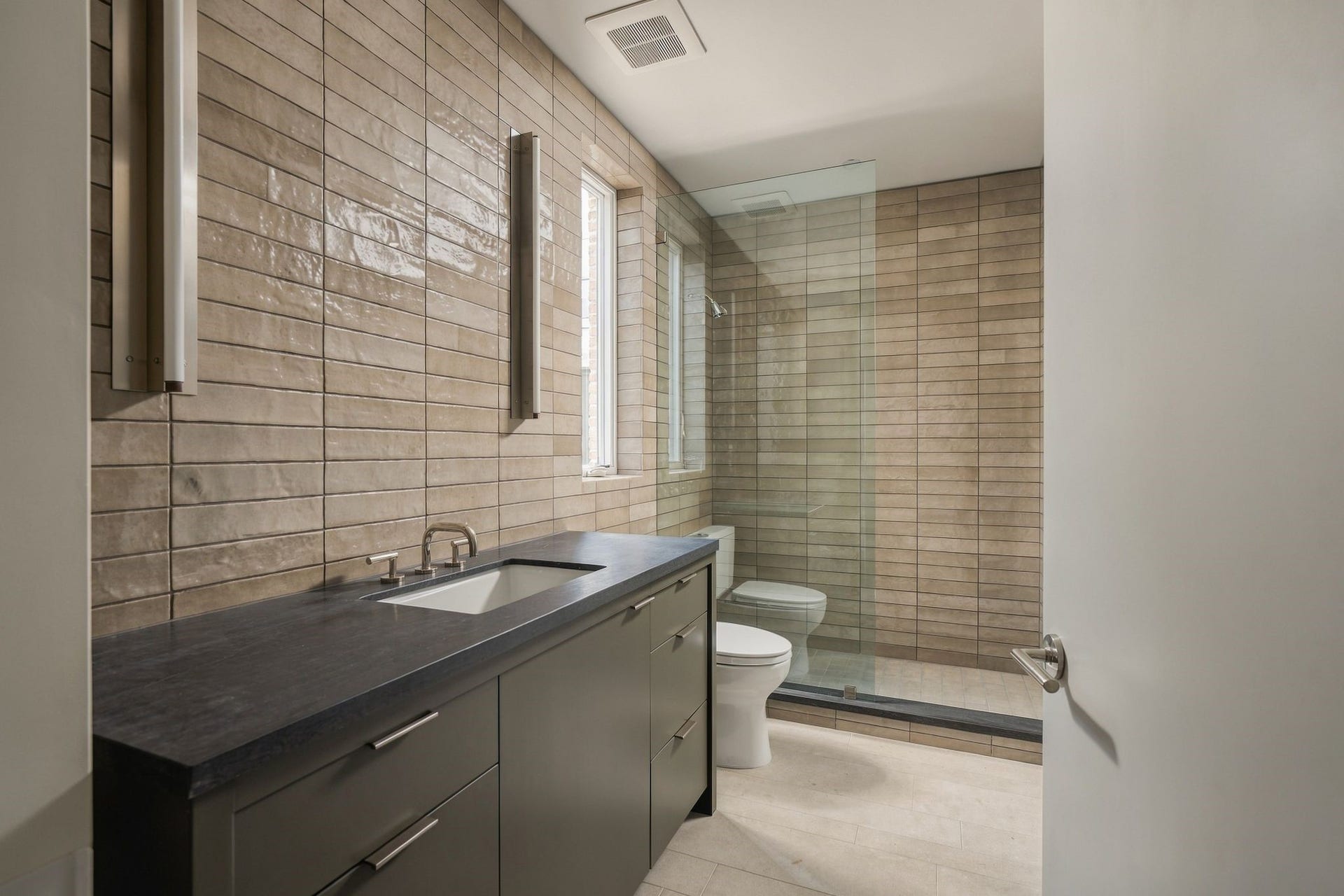 Private en suite bath serving the first-floor flex/5th bedroom features limestone flooring, Juniper lighting & a walk-in shower w/porcelain tile walls, frameless glass & built-in niche. A custom walk-in closet w/built-in dresser is conveniently tucked just beyond.