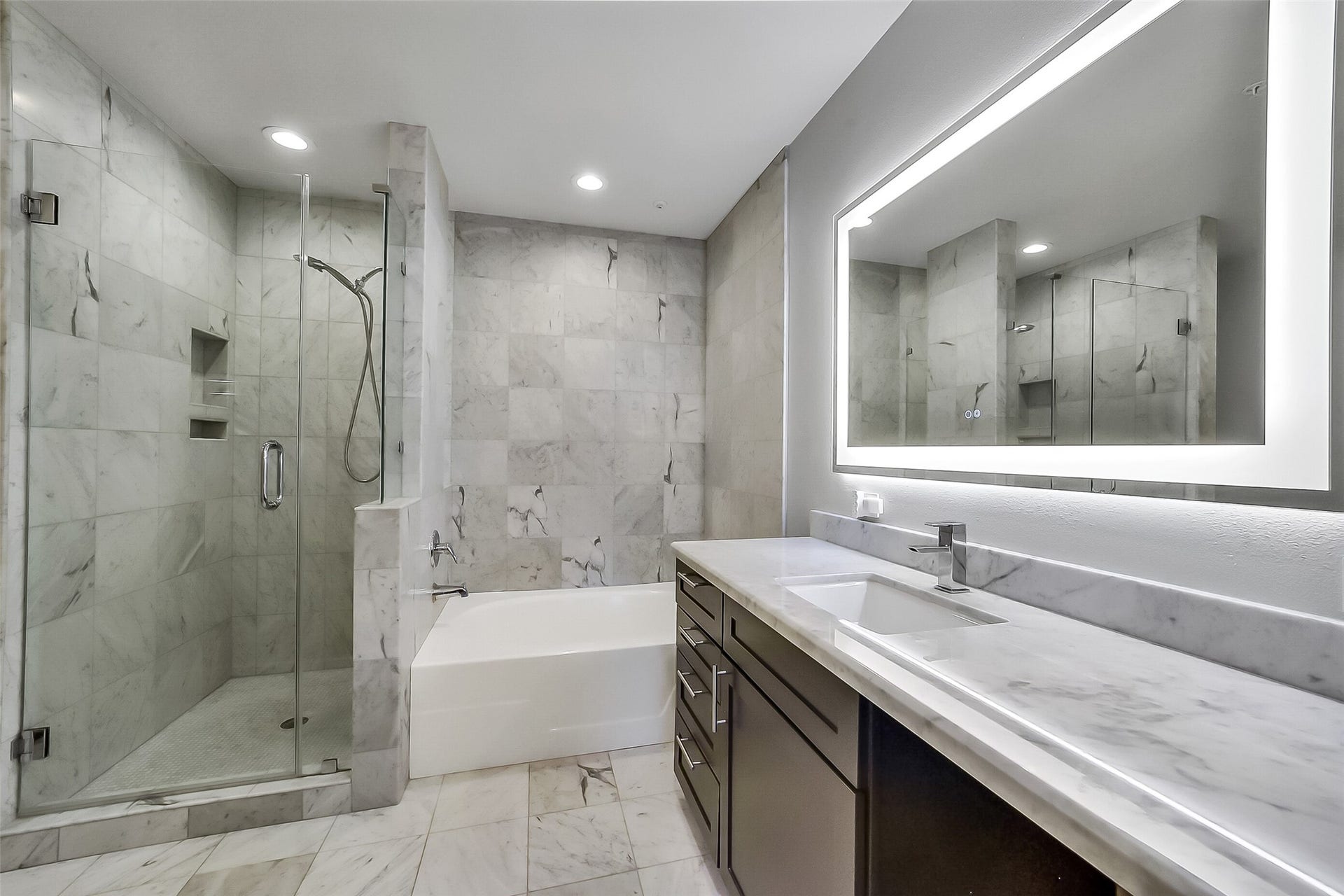 3333 Allen Parkway, #710, Houston, TX 77019 The ensuite primary bathroom basks in gleaming white, featuring a frameless glass shower and a separate bath tub. Down lights and illuminated mirrors add to the elegance.