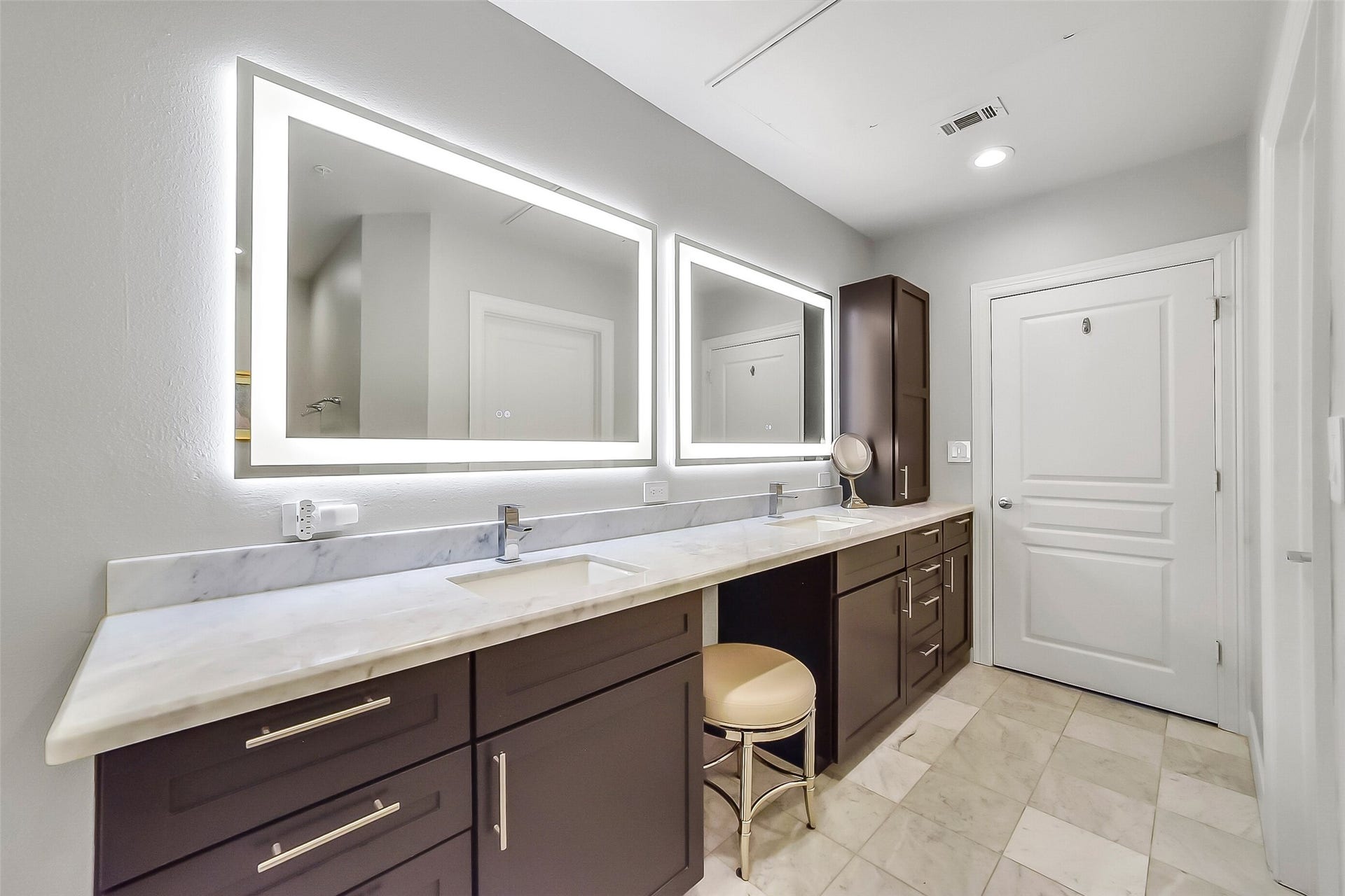 3333 Allen Parkway, #710, Houston, TX 77019 Double sinks and illuminated mirrors are complemented by cabinets, whose saturated brown contrasts the gleaming white floor and countertop.
