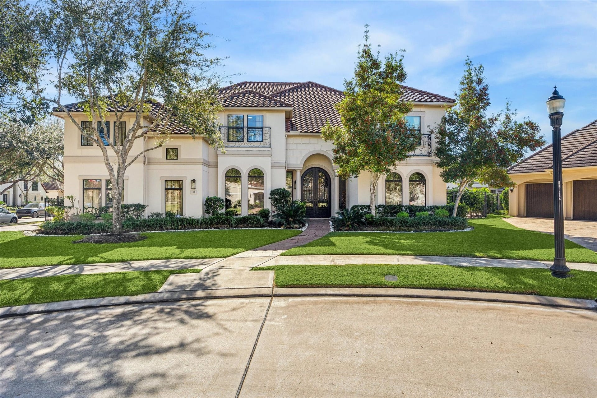 61 Open Sands Court, Sugar Land, TX 77479 This stunning two-story home features a Mediterranean-inspired design with a tiled roof and arched windows. The manicured front lawn, framed by mature trees and lush landscaping, enhances its curb appeal. A spacious driveway leads to a three-car garage, offering ample parking and storage.