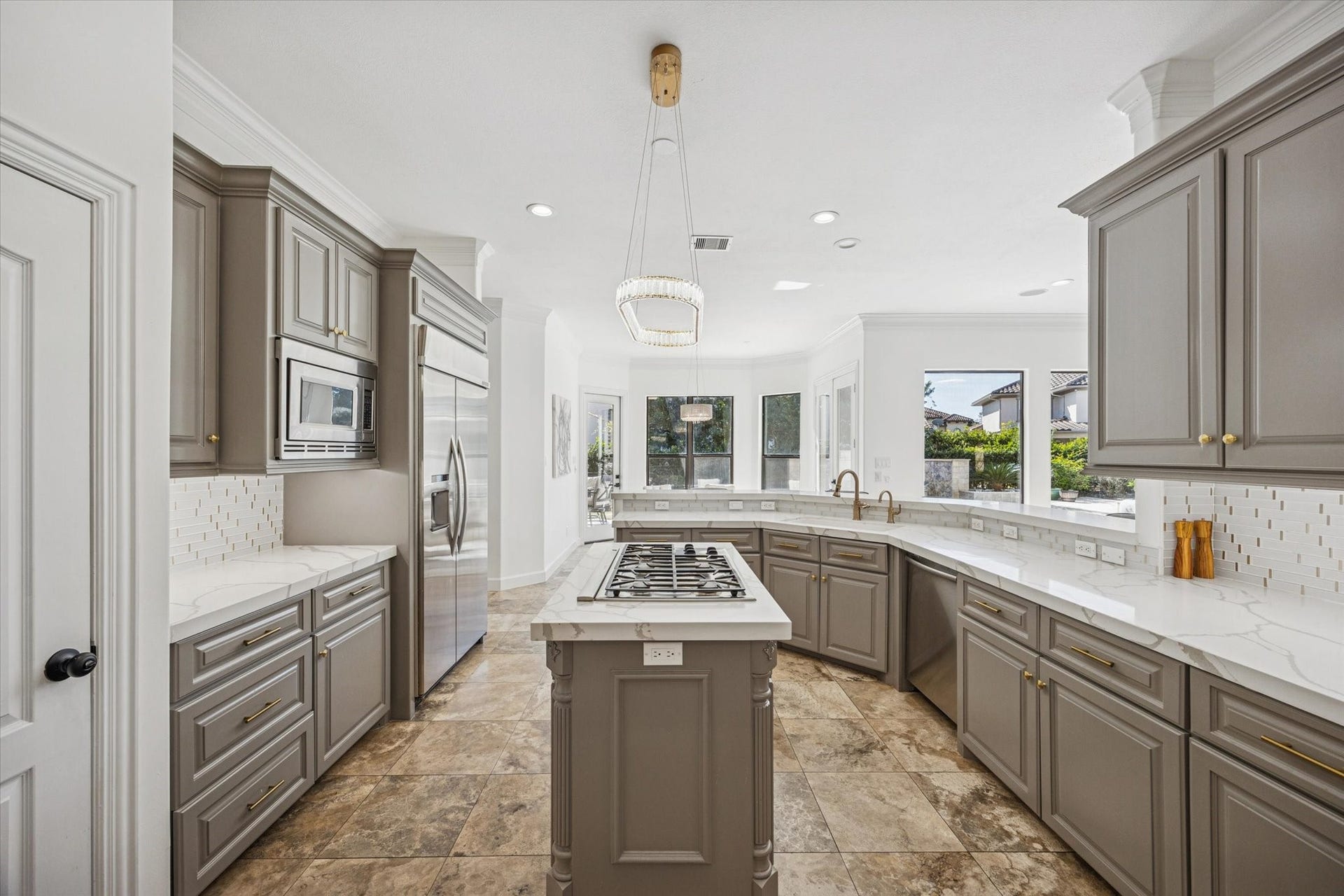 61 Open Sands Court, Sugar Land, TX 77479 This spacious kitchen features elegant gray cabinetry, a large central island with a gas cooktop, and modern stainless steel appliances. The room is brightened by ample natural light from large windows, highlighting the sleek tile flooring and contemporary lighting fixture.