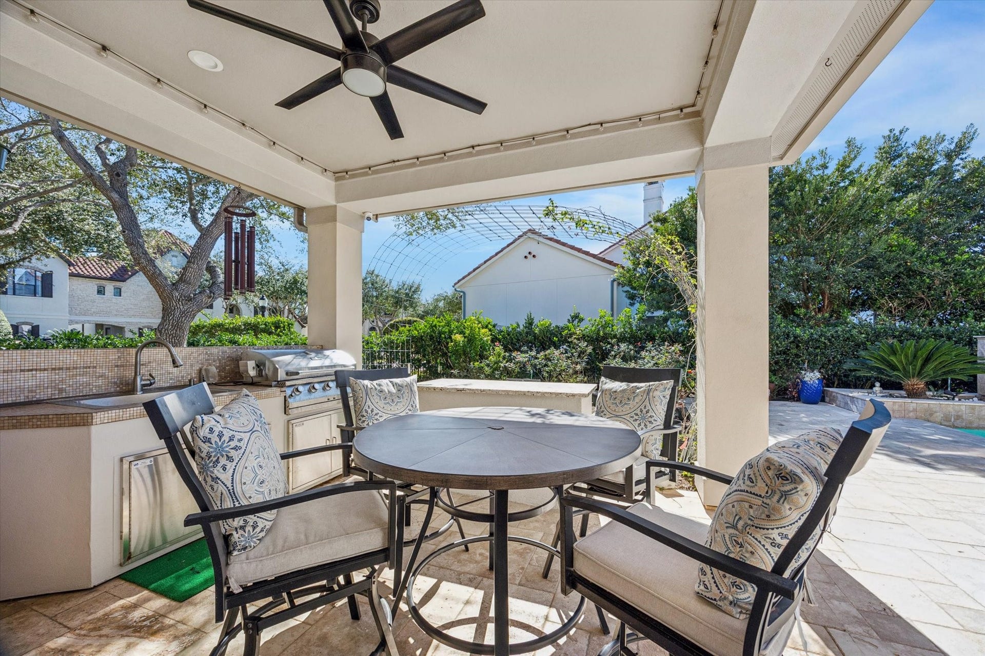 61 Open Sands Court, Sugar Land, TX 77479 This photo showcases a stylish outdoor patio with a covered seating area, It features an outdoor kitchen with a built-in grill and sink, surrounded by lush greenery. The space offers a perfect setting for entertaining and relaxation.