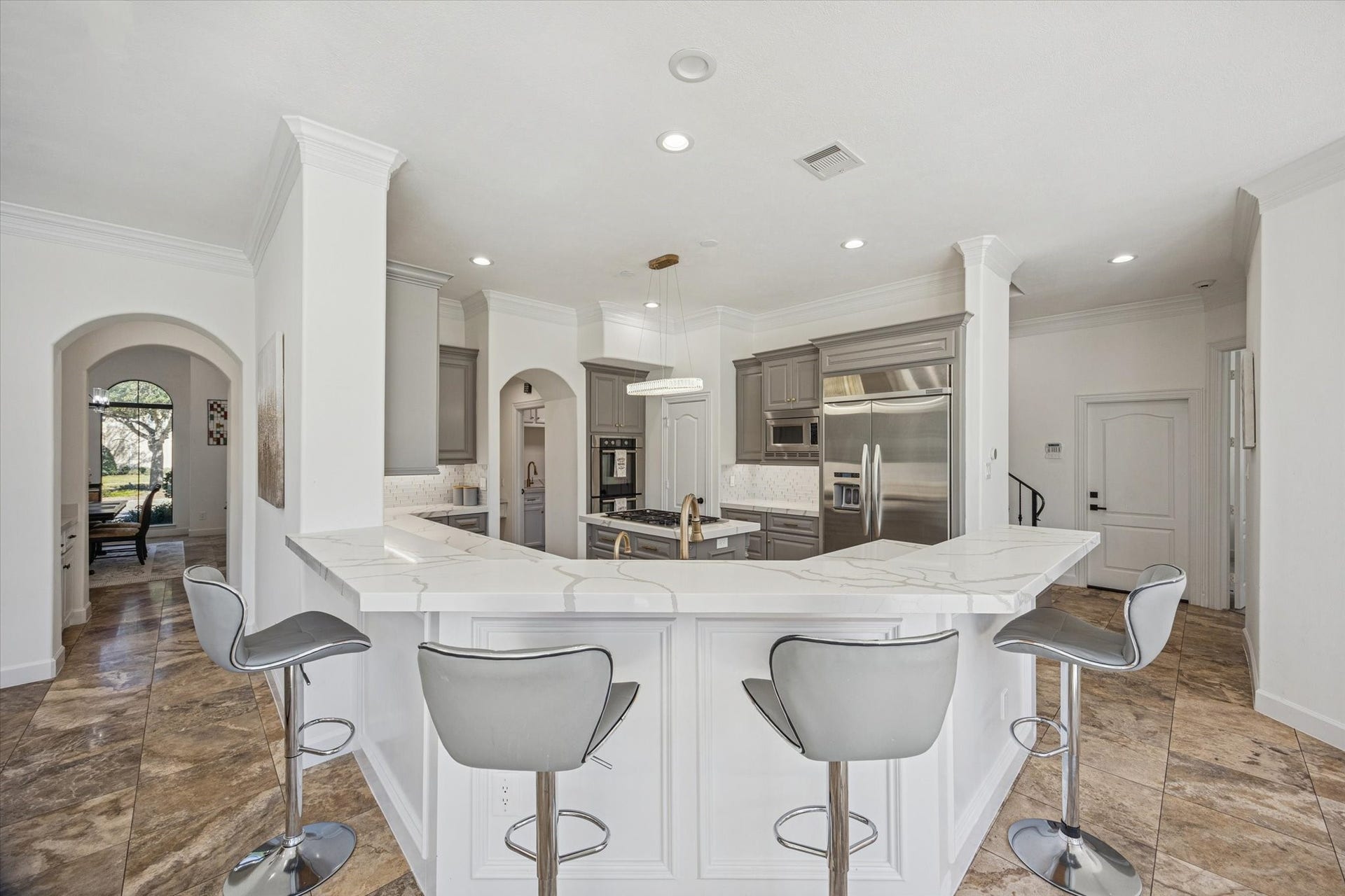 61 Open Sands Court, Sugar Land, TX 77479 This modern kitchen features a spacious, open design with a large island and sleek bar seating. It includes stainless steel appliances, elegant cabinetry, and ample counter space, complemented by recessed lighting and tile flooring. An arched entryway leads to an adjacent room, enhancing the open flow.