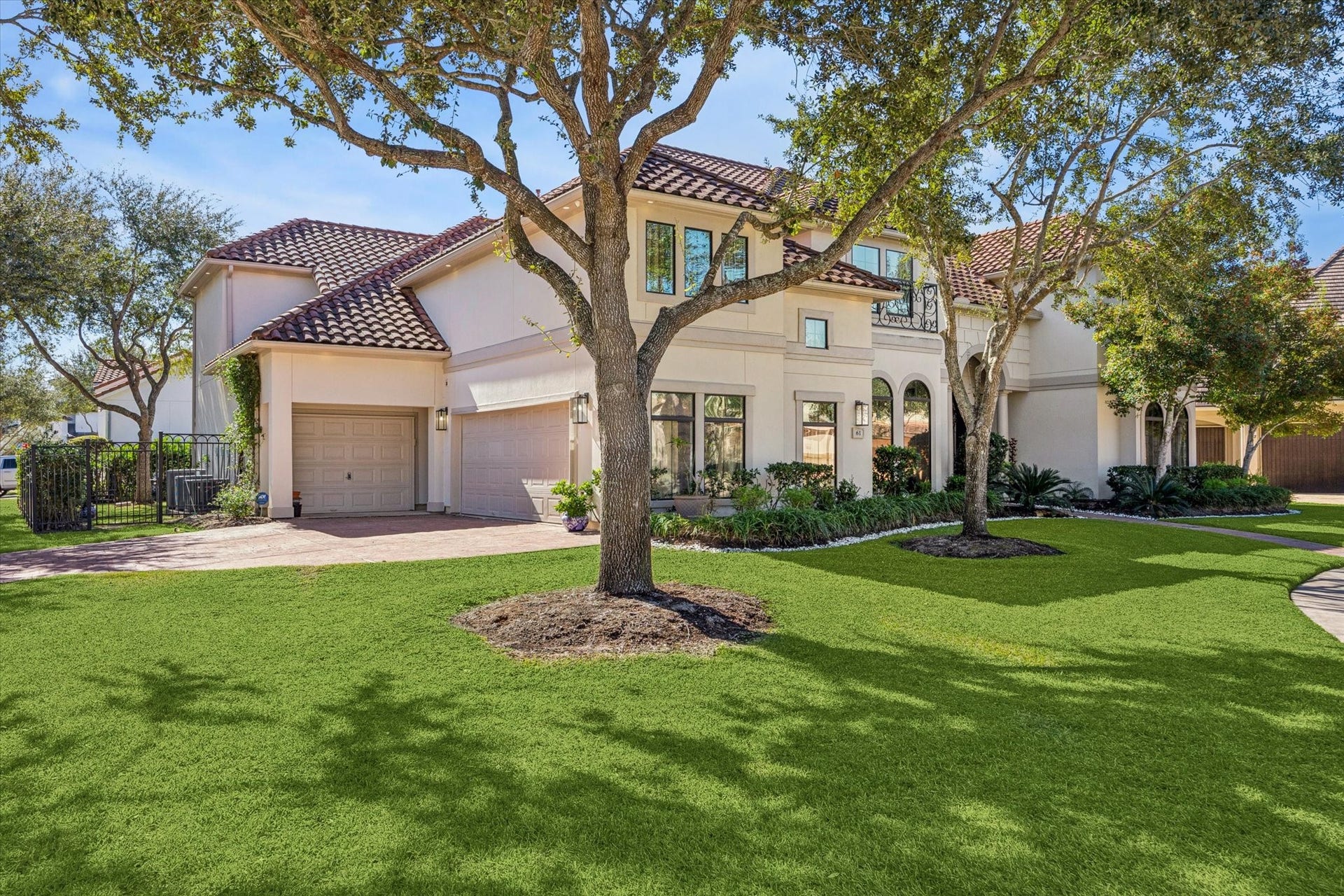 61 Open Sands Court, Sugar Land, TX 77479 This photo shows a spacious two-story home with a tile roof, large windows, and a well-maintained front yard with mature trees. The driveway leads to a three-car garage Home located on a corner of a cup-de-sac street.