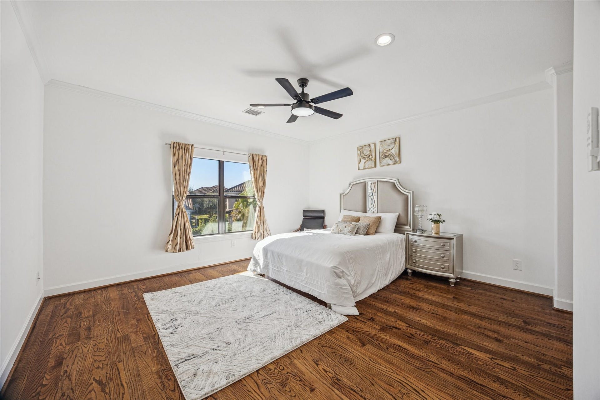 61 Open Sands Court, Sugar Land, TX 77479 This is a bright, spacious upstairs bedroom featuring hardwood floors, a ceiling fan, and a large window with drapes.