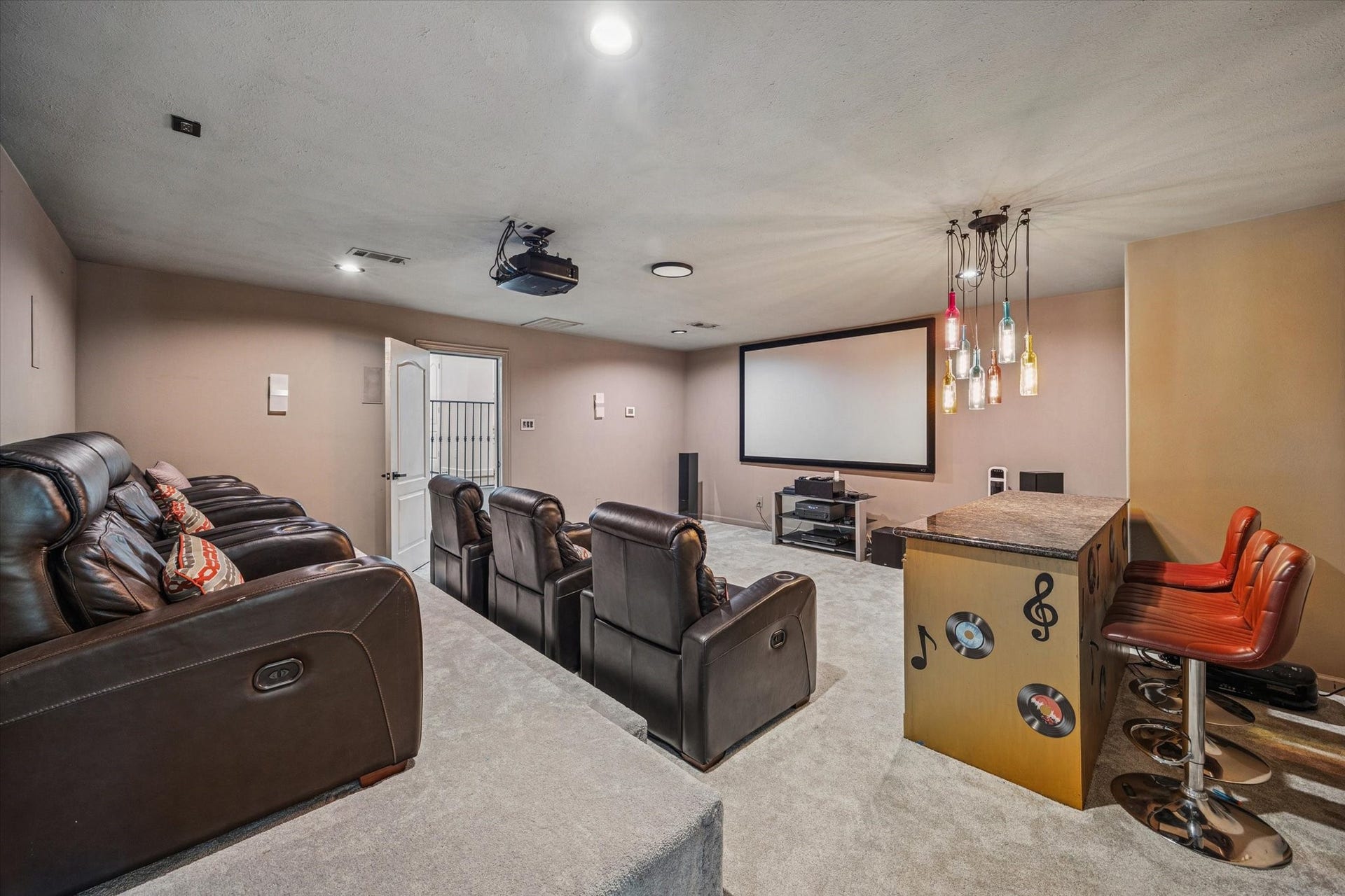 61 Open Sands Court, Sugar Land, TX 77479 This photo showcases a home theater room with tiered leather recliners, a large projection screen, and a cozy bar area with modern lighting and seating. Perfect for entertaining and movie nights.
