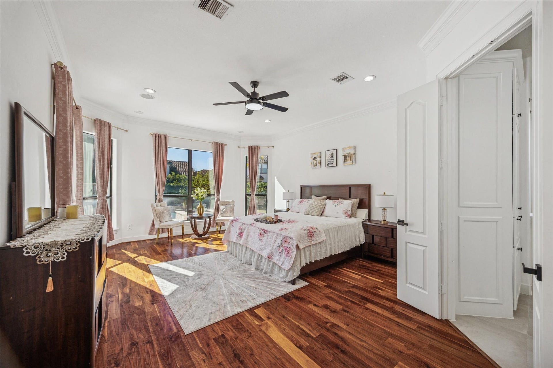 61 Open Sands Court, Sugar Land, TX 77479 This spacious, bright primary bedroom features hardwood floors, large windows with elegant curtains, and a ceiling fan. It includes a cozy sitting offering a warm and inviting atmosphere.