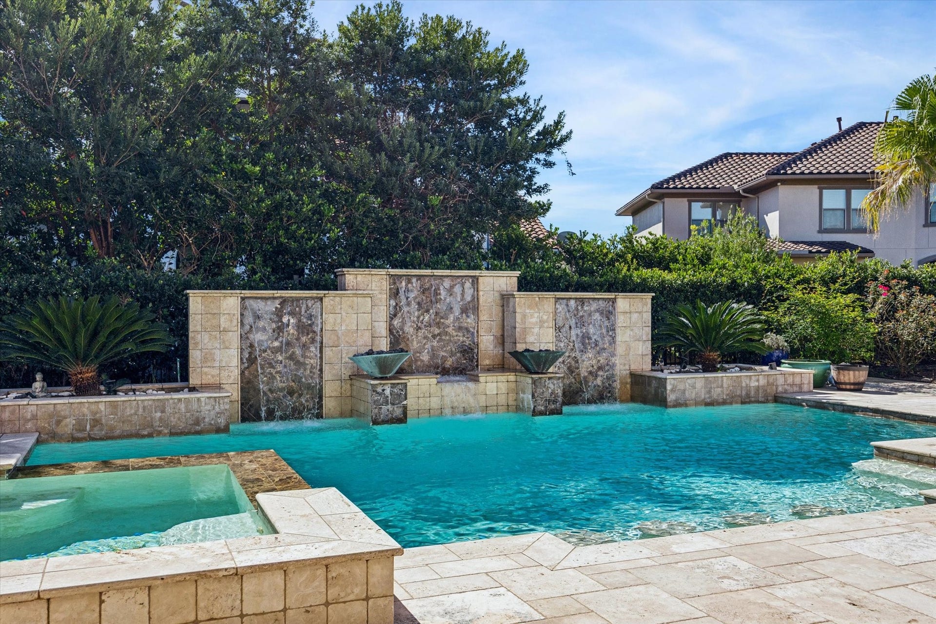 61 Open Sands Court, Sugar Land, TX 77479 This photo showcases a luxurious backyard with a stunning pool featuring elegant water features and a spa, surrounded by lush greenery and a stylish tile deck, perfect for relaxation and entertainment.
