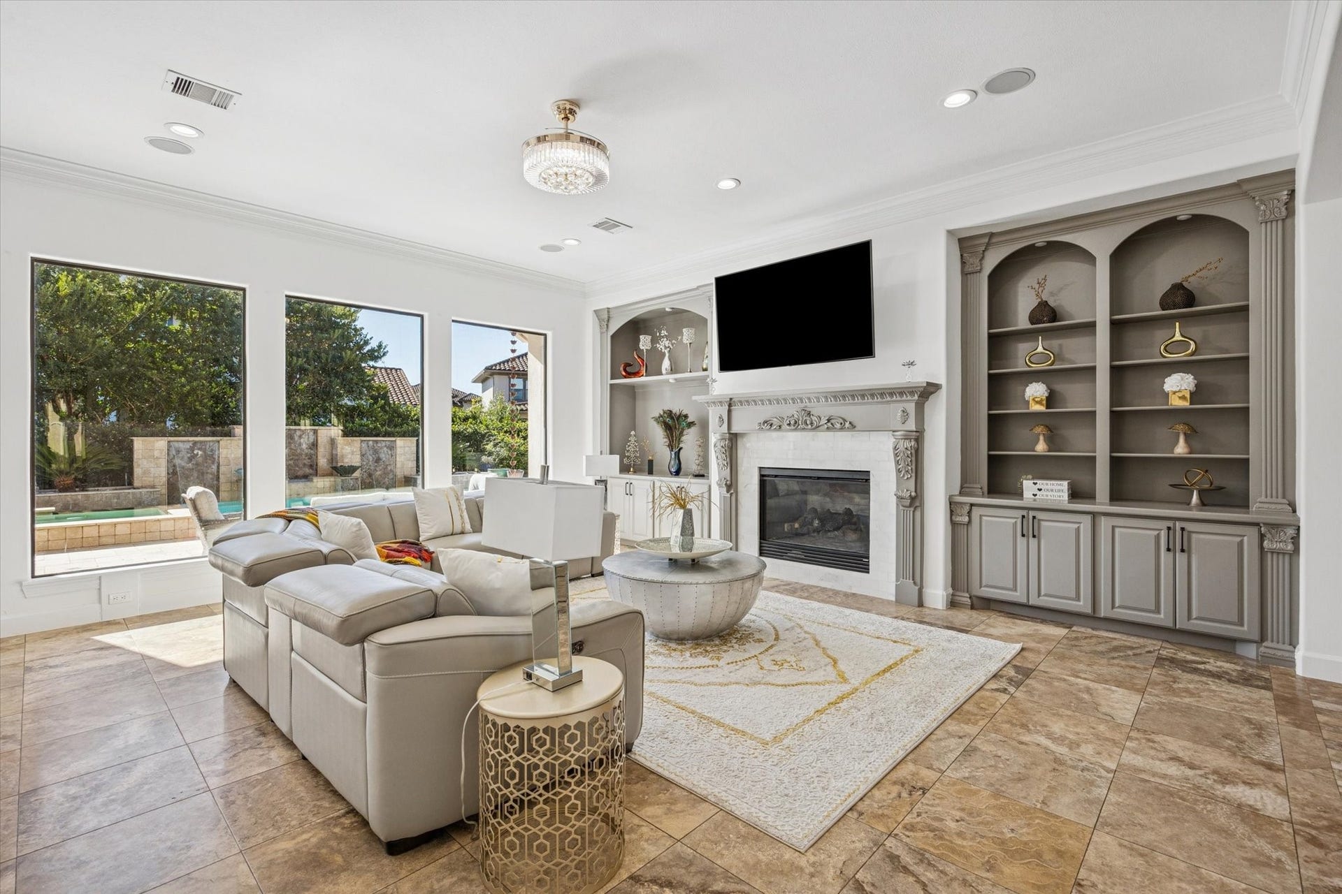 61 Open Sands Court, Sugar Land, TX 77479 This spacious living room features elegant travertine tile flooring, a cozy fireplace, and built-in shelving. Large windows offer abundant natural light and a view of the outdoor pool area.
