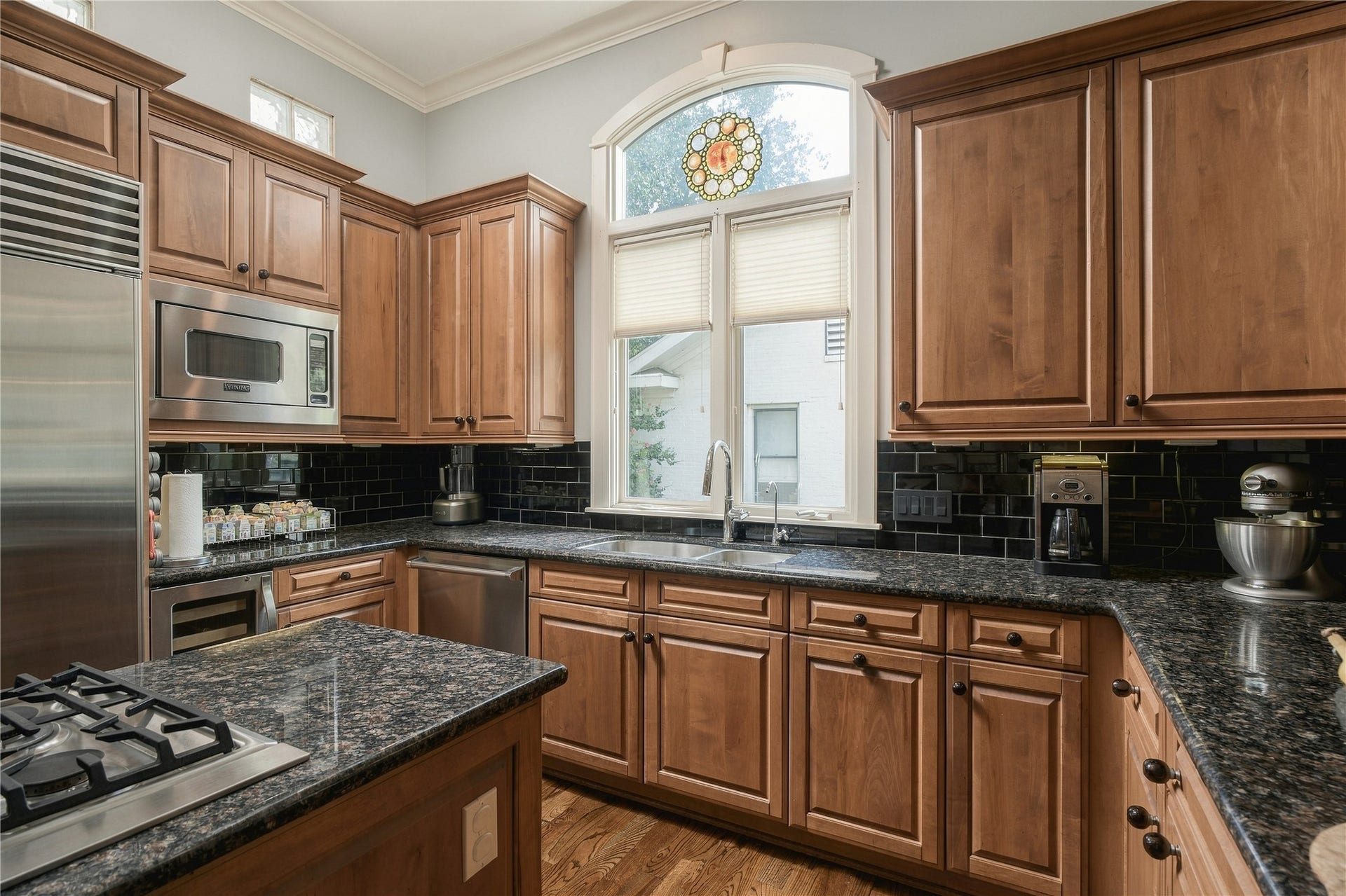 523 Lovett Boulevard, Houston, TX 77006 The kitchen shifts the palette warmer with rich wood cabinetry, dark granite surfaces and a black tile backsplash, while an arched window brings natural light over the sink.