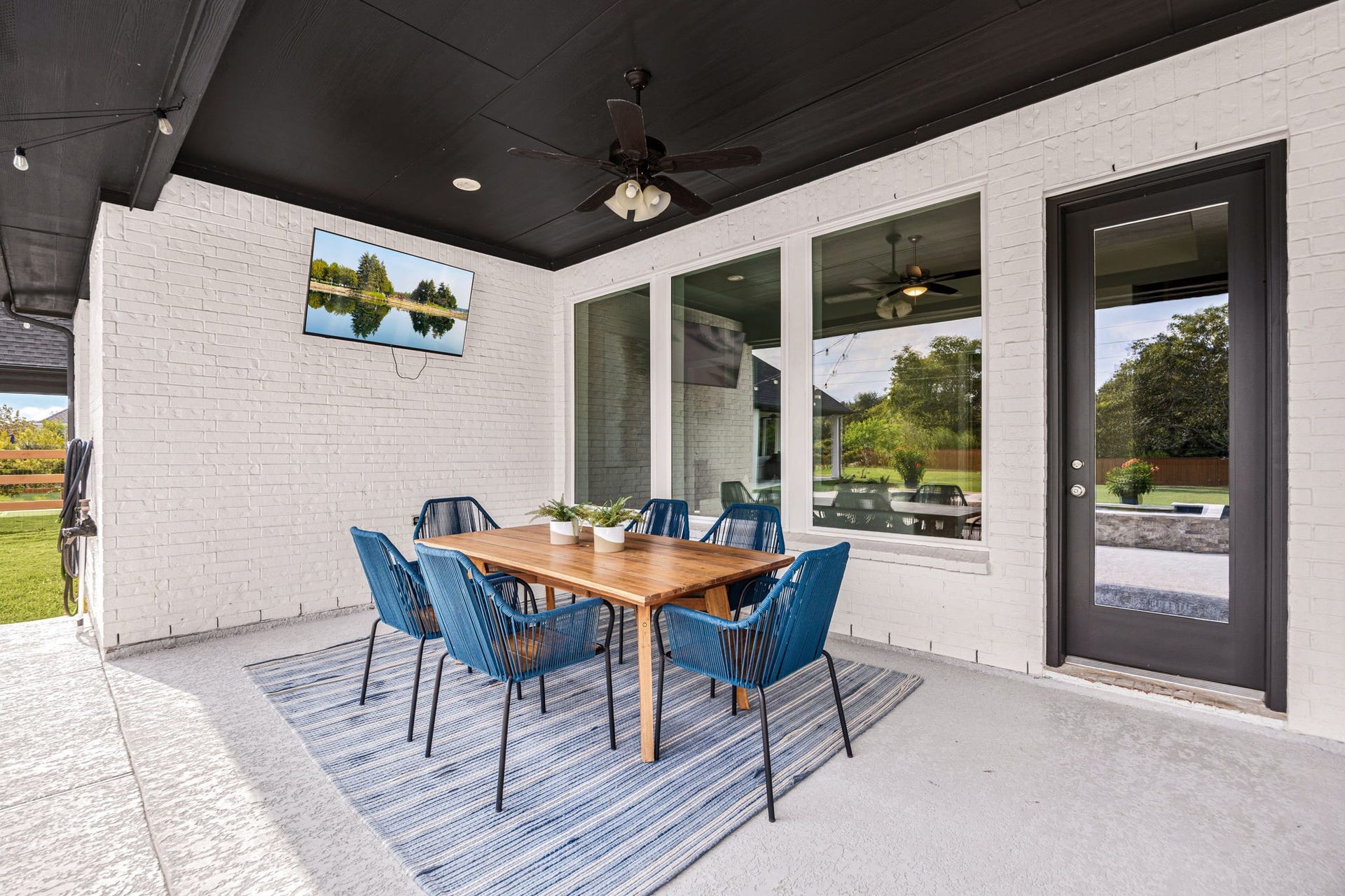The covered patio creates a comfortable extension of the home with room for outdoor dining and lounging. It is complete with ceiling fans and a mounted TV, all overlooking the pool and the back half of the acre lot.