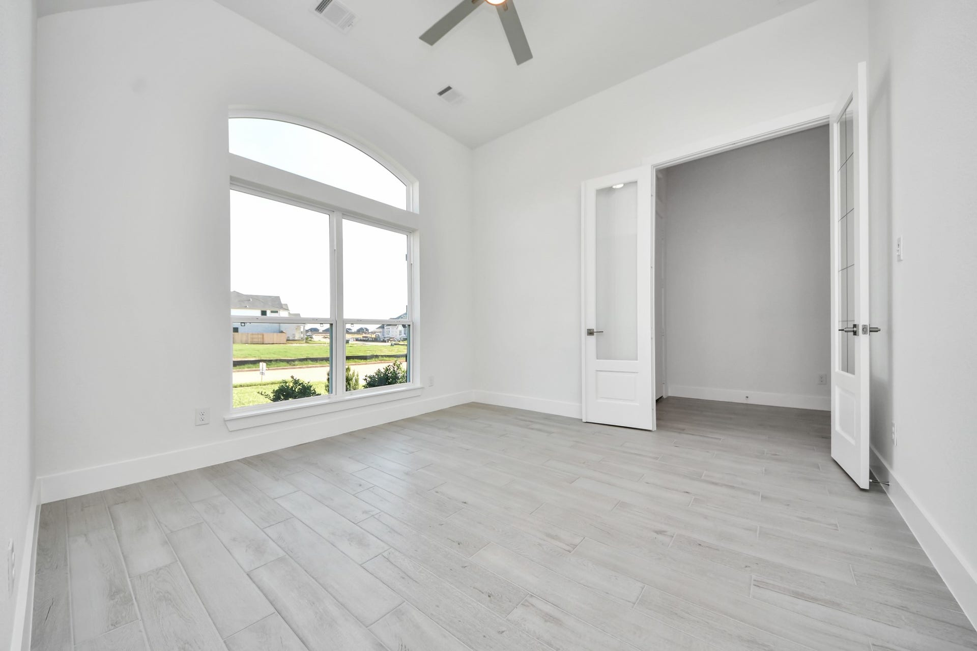 Experience the perfect blend of sophistication and warmth in this home office, boasting elegant wood-look tile flooring and flooded with natural light from expansive windows and French doors.