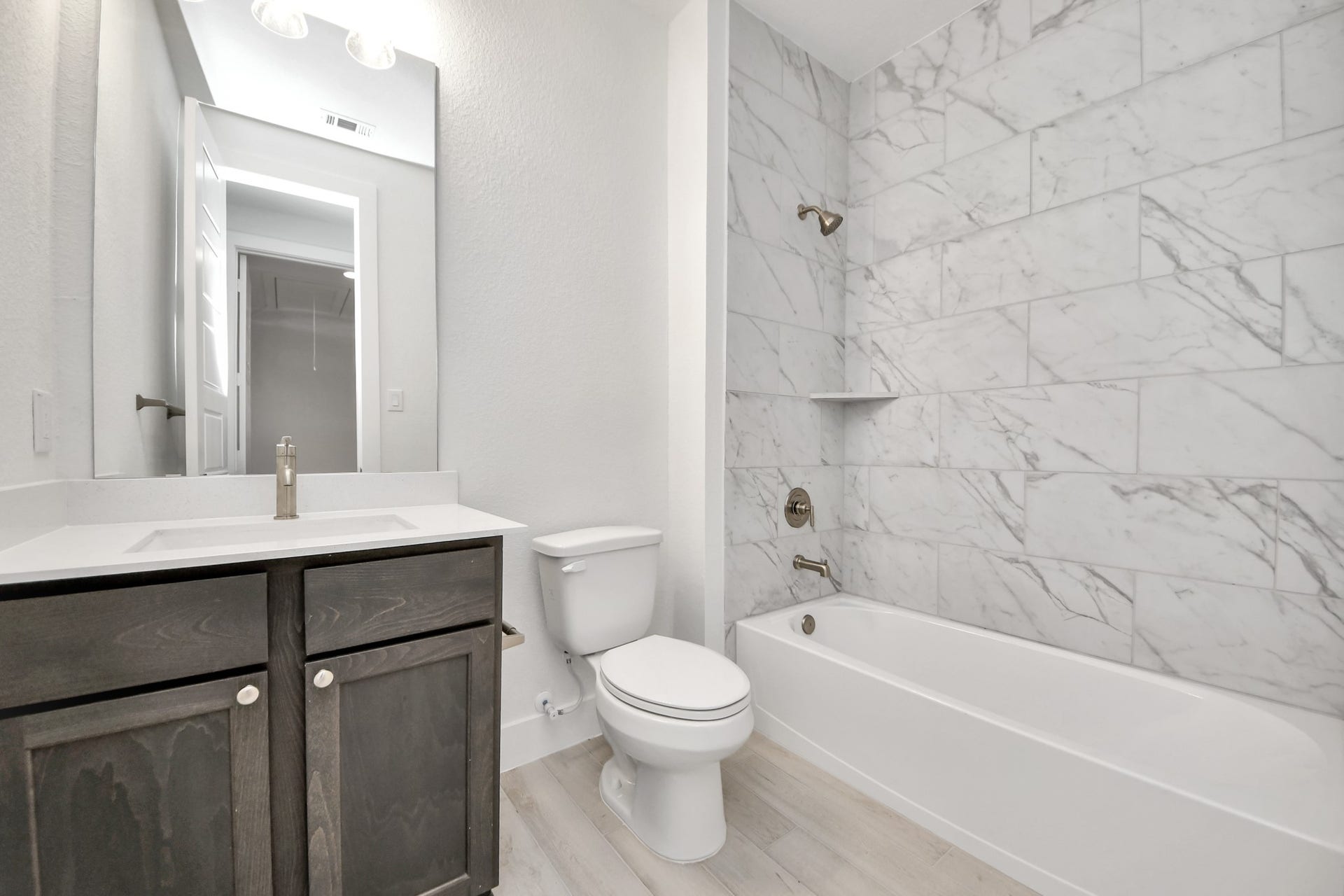 Secondary bath features tile flooring, bath/shower combo with tile surround, light stained wood cabinets, beautiful light countertop.