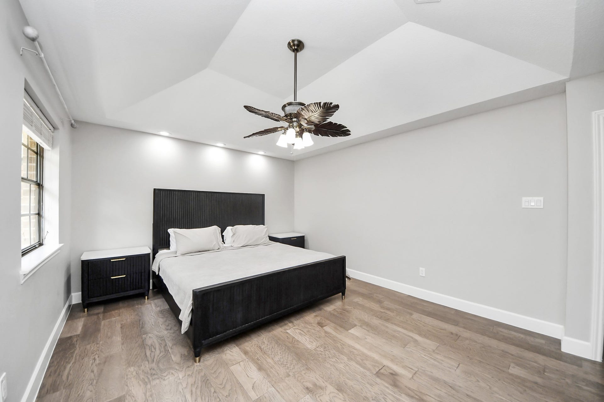 24 Hornsilver Place, The Woodlands, TX 77381 Spacious bedroom with sleek modern design, featuring a vaulted ceiling, elegant light fixture, and abundant natural light from the large window.