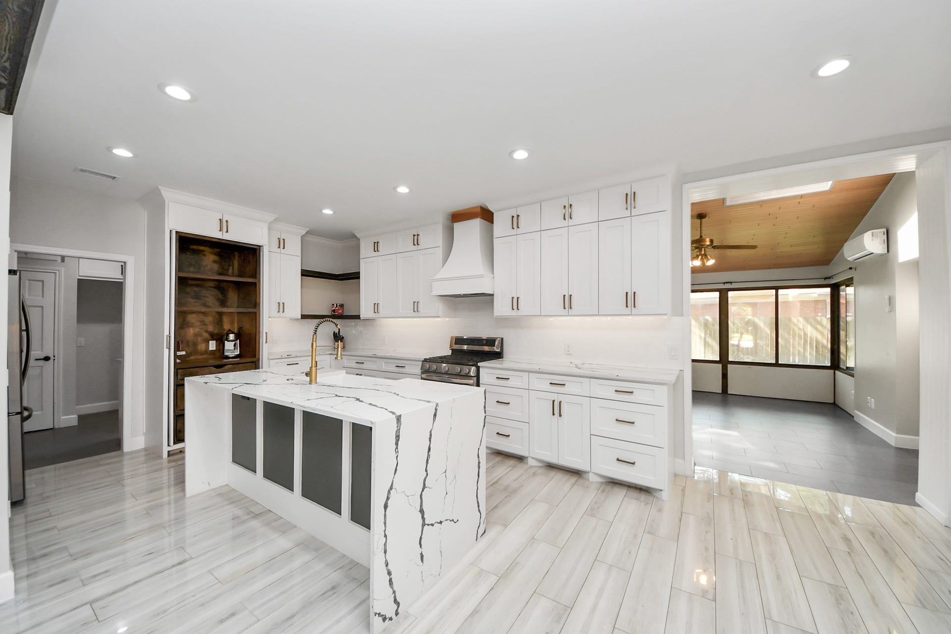 24 Hornsilver Place, The Woodlands, TX 77381 Sleek, modern kitchen with a striking waterfall island, elegant white cabinetry, and stainless steel appliances, seamlessly connected to a bright, inviting sunroom.