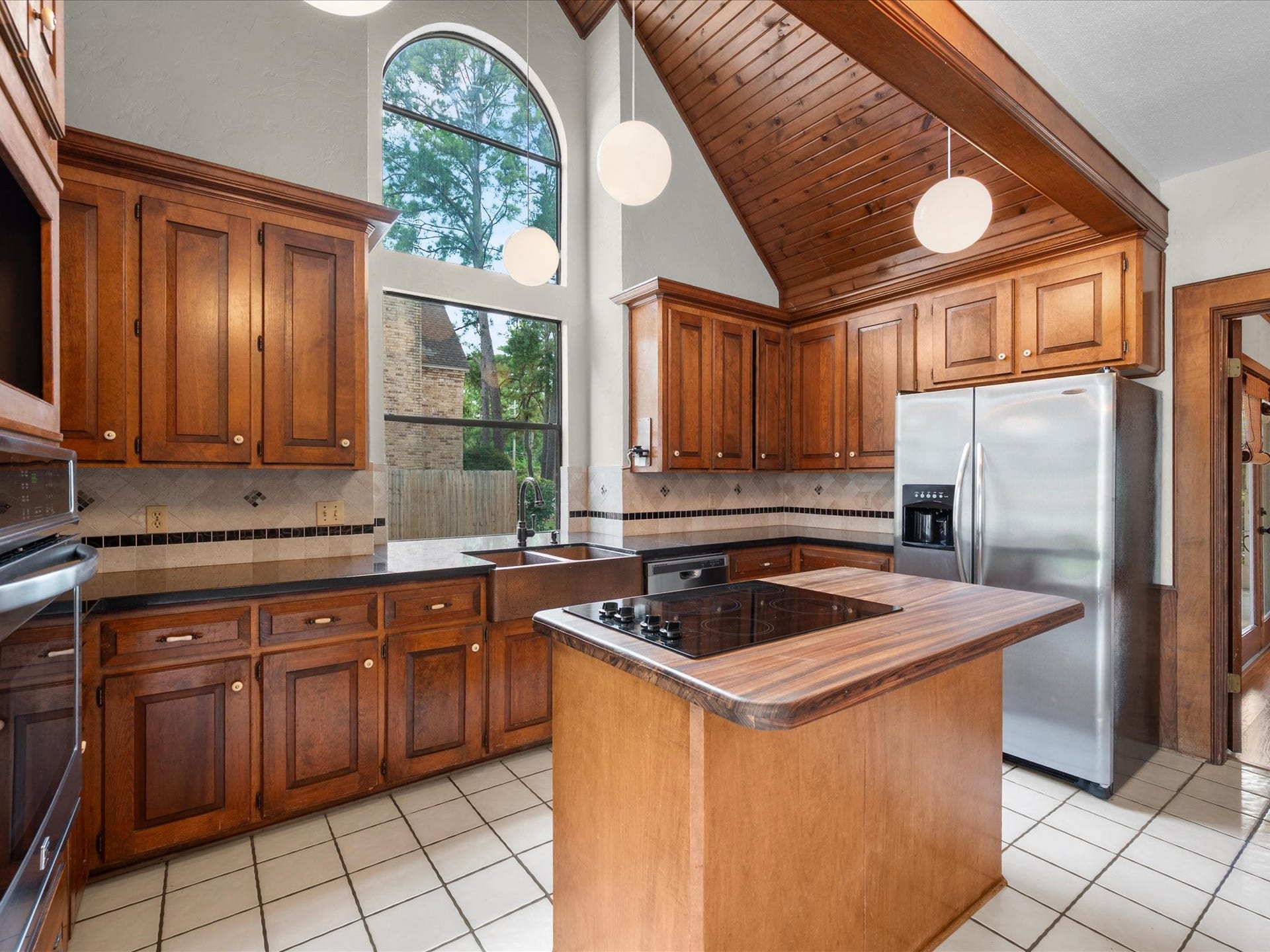 18006 Memorial Estates Drive, Spring, TX 77379 The kitchen sits under a vaulted wood ceiling with an arched window up high. The island has a gas cooktop built in.