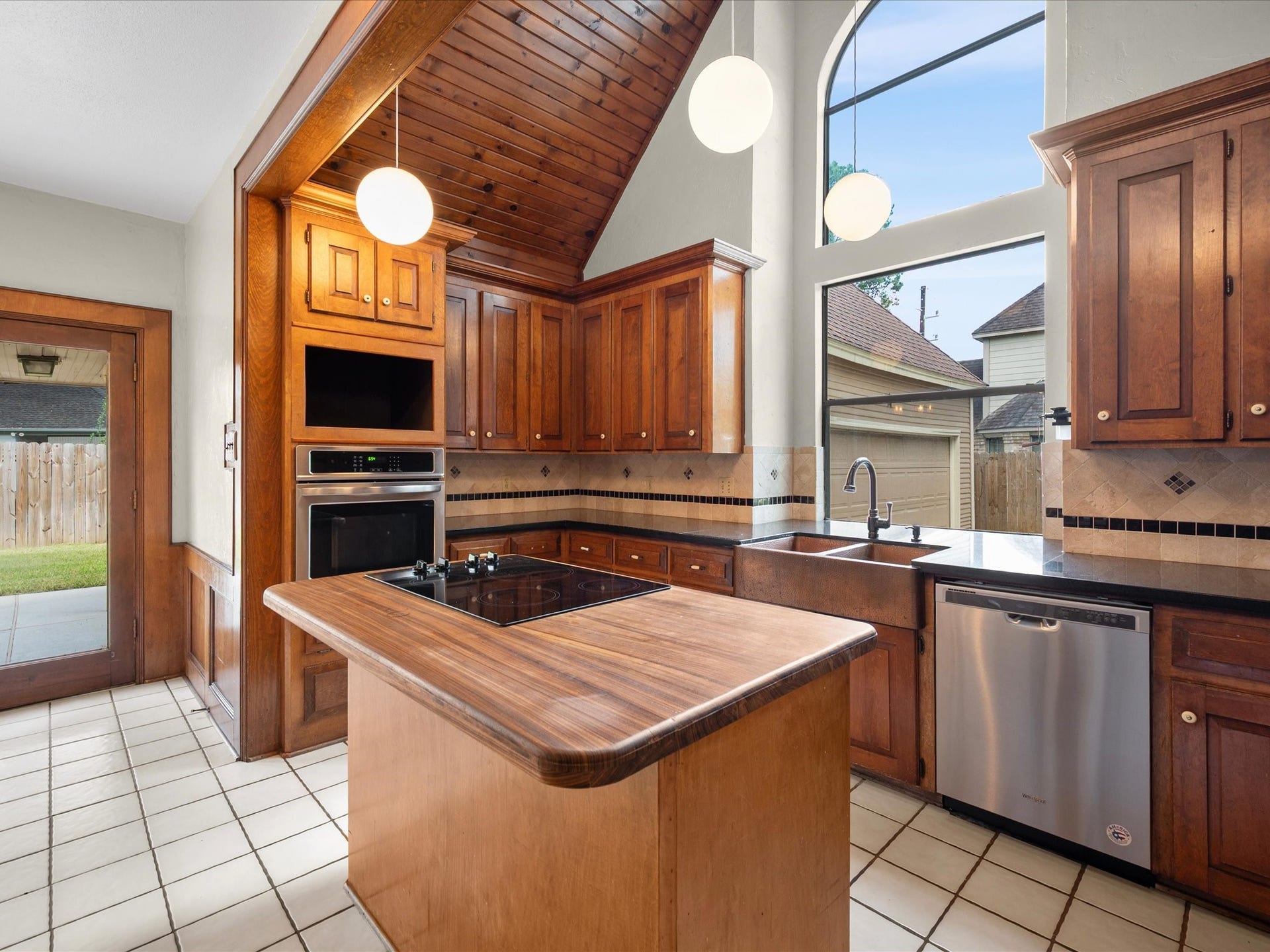 18006 Memorial Estates Drive, Spring, TX 77379 Wall oven, dishwasher, and an island with a gas cooktop. Pendant lights hang from the vaulted wood ceiling.