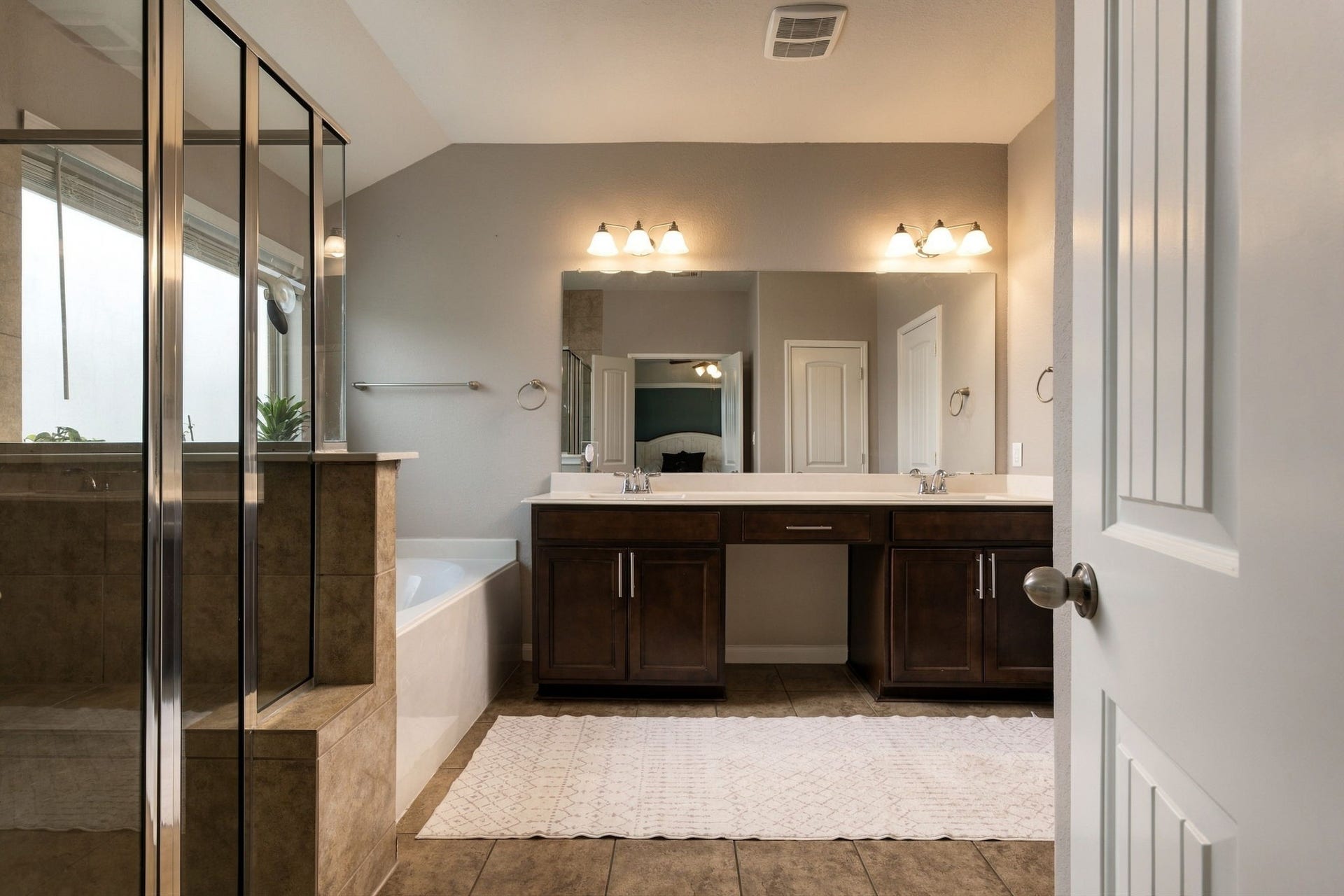 336 Country Crossing Circle, Magnolia, TX 77354 Spacious bathroom featuring a double vanity with elegant lighting, a large mirror, and a glass-enclosed shower next to a relaxing bathtub.