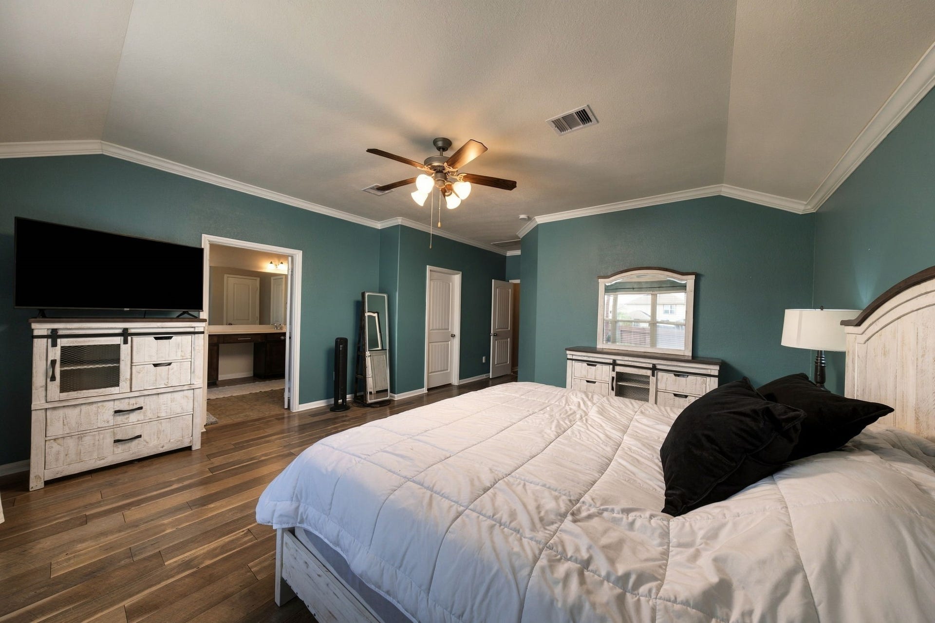 336 Country Crossing Circle, Magnolia, TX 77354 Spacious bedroom with rich teal walls, elegant crown molding, and warm wood flooring. Features include a ceiling fan, ample natural light from a large window offering a cozy and inviting retreat.