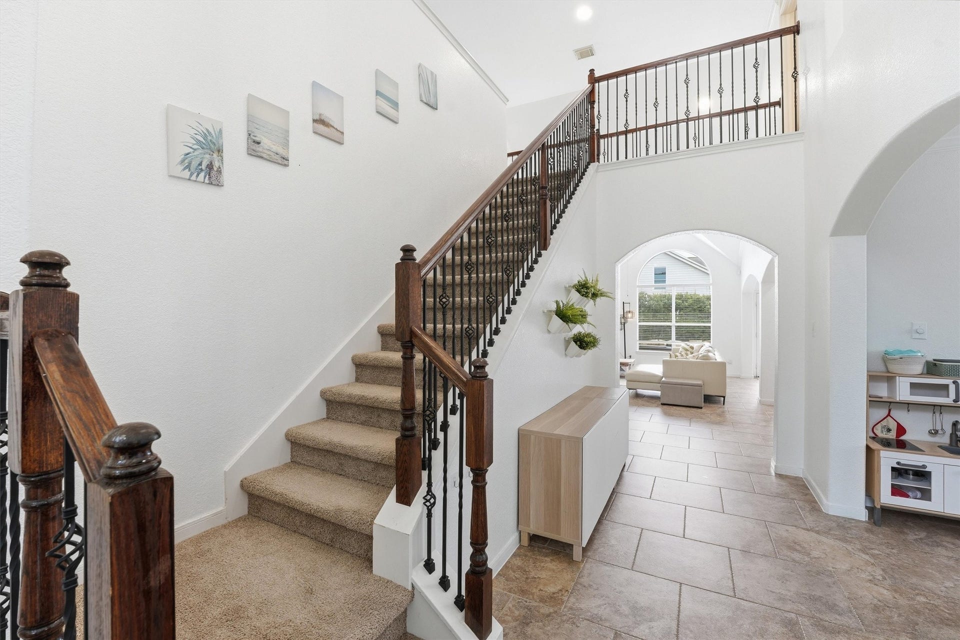 This welcoming entryway features elegant tile flooring and a carpeted staircase with wooden and wrought iron railing. The bright space leads to an open living area through a graceful archway, and includes a side room with French doors.