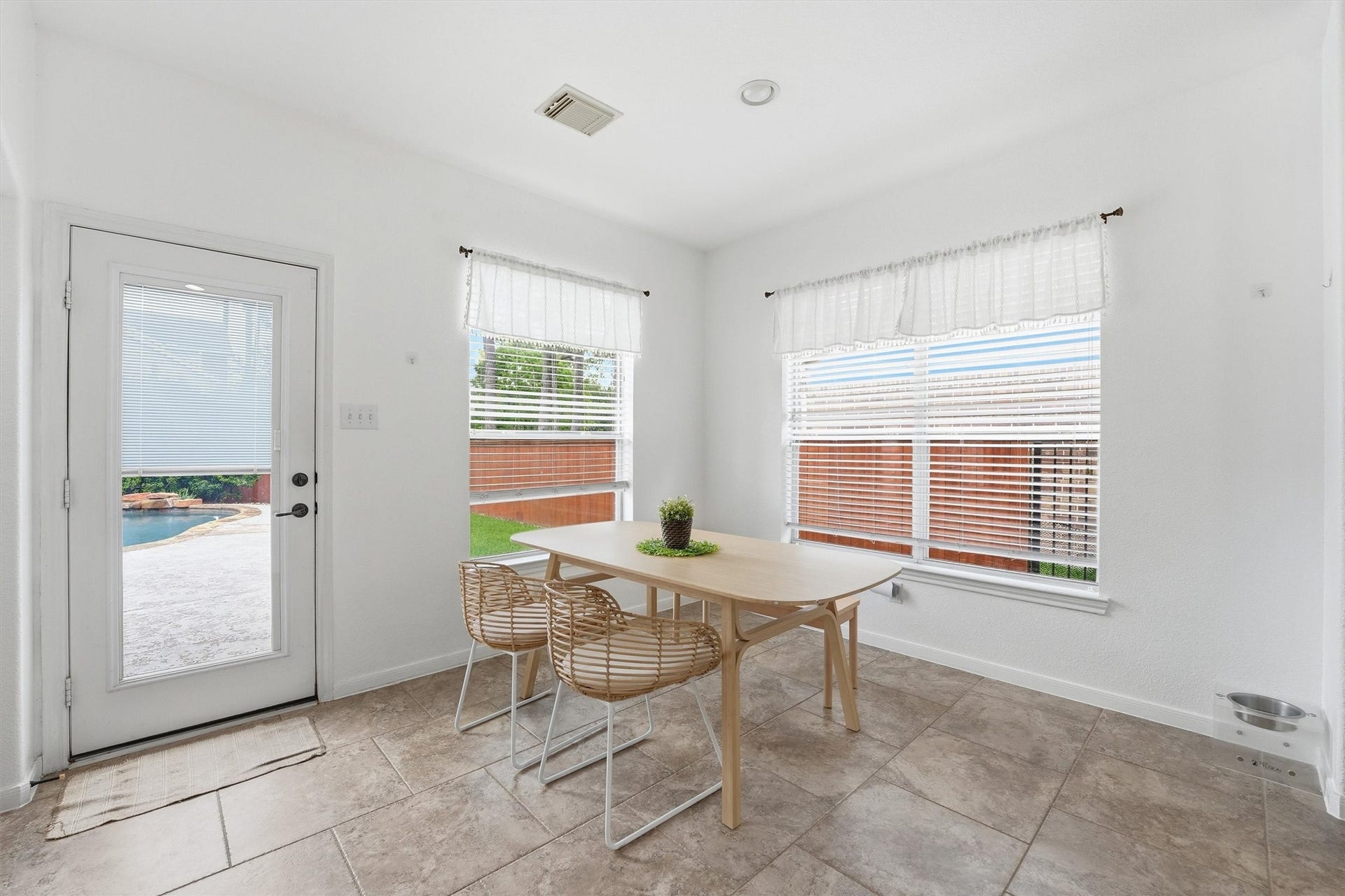 This photo showcases a bright, open-concept living area with a modern kitchen featuring a large island and stainless steel appliances. The room flows into a cozy living space with a fireplace and a wall-mounted TV. Large windows and a glass door provide ample natural light and access to a patio.